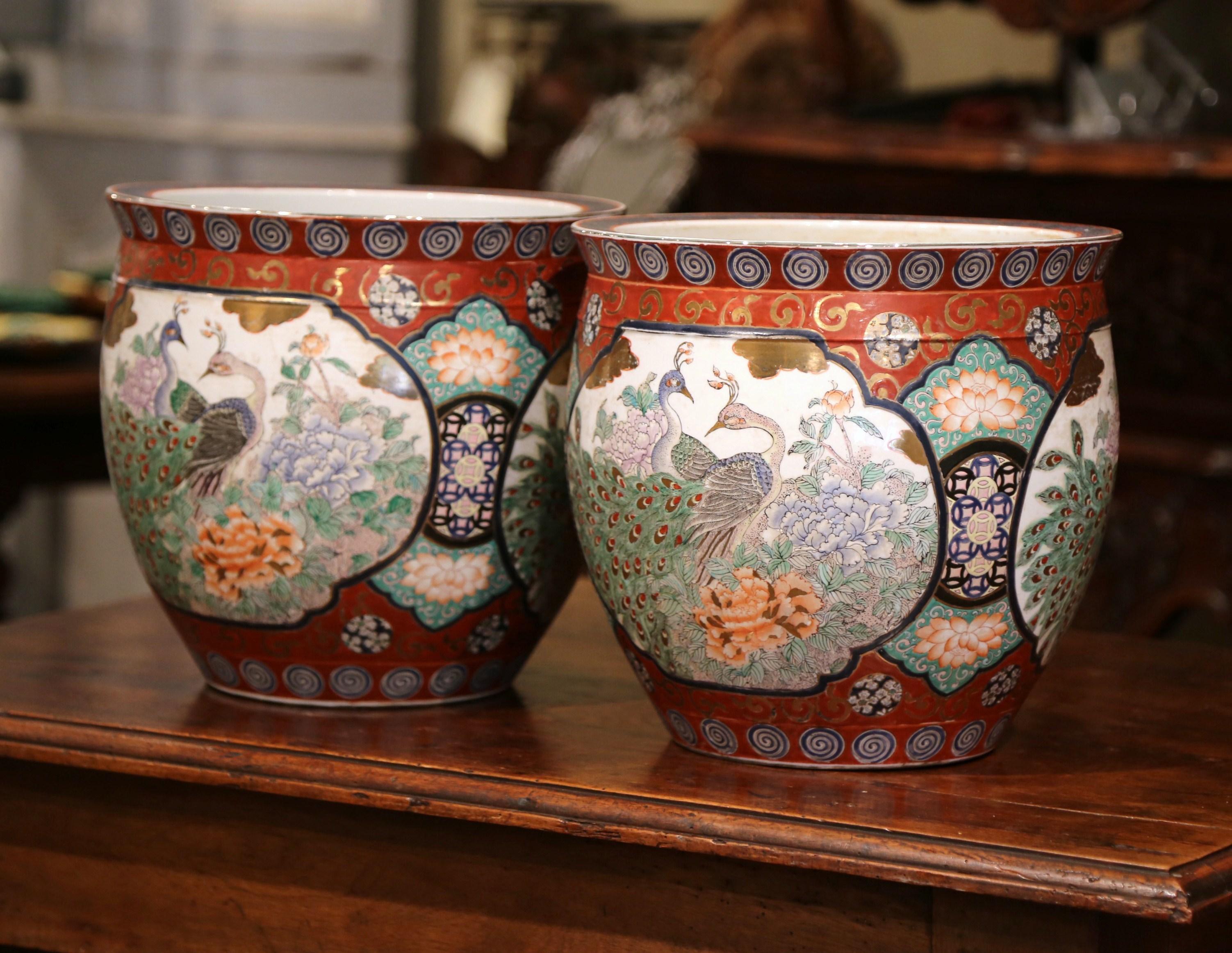 Crated in China, circa 1920, each porcelain planter is hand painted with peacock medallions and floral decor, and embellished with gilt motifs. The pots are in excellent condition, signed on the bottom and adorn rich colors in the red palette. Fill