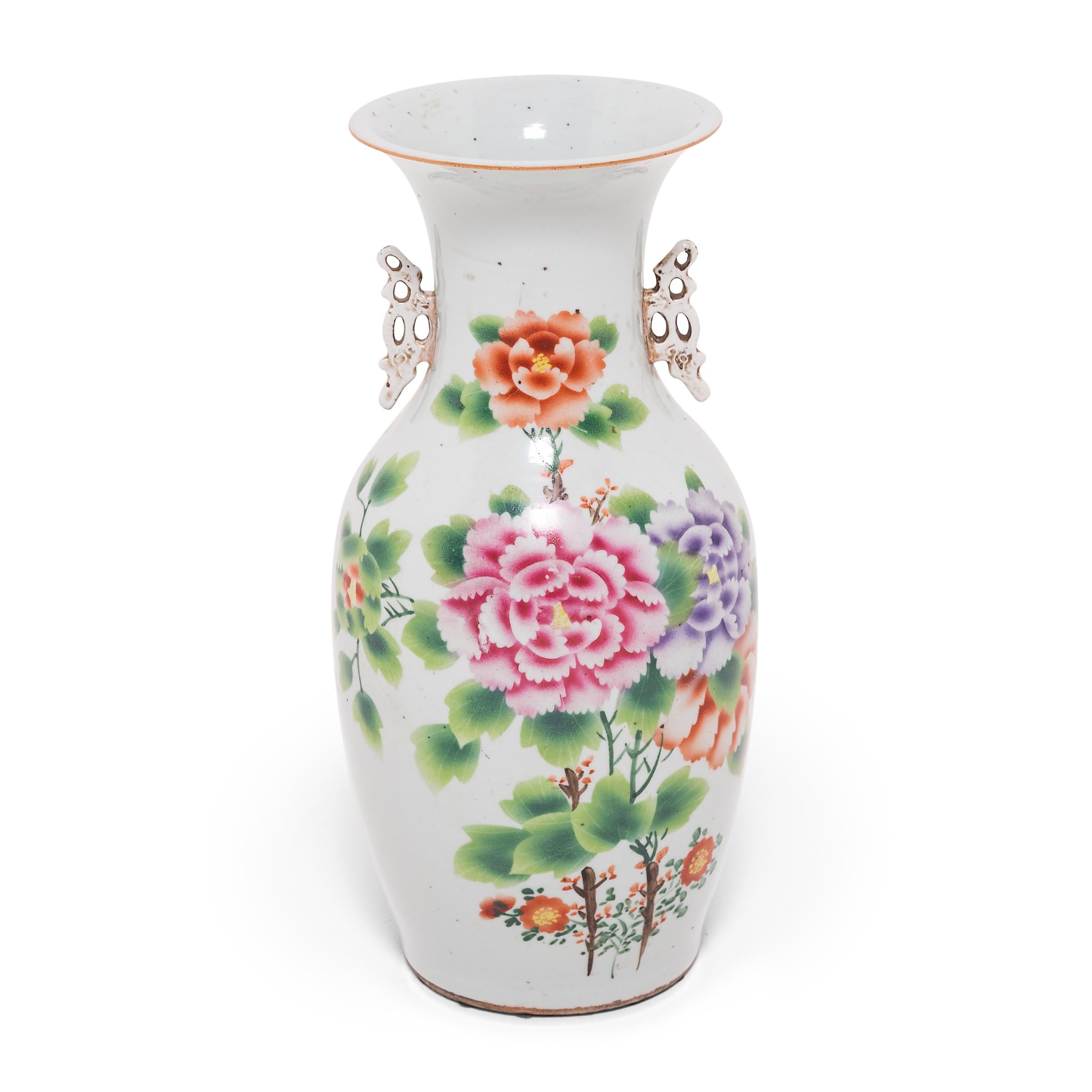 Questa coppia di vasi in porcellana, splendente di fiori lussureggianti e colori brillanti, combina la lavorazione a stencil con il fogliame dipinto a mano in uno stile decorativo popolare nei primi due decenni del XX secolo. I petali e i fiori