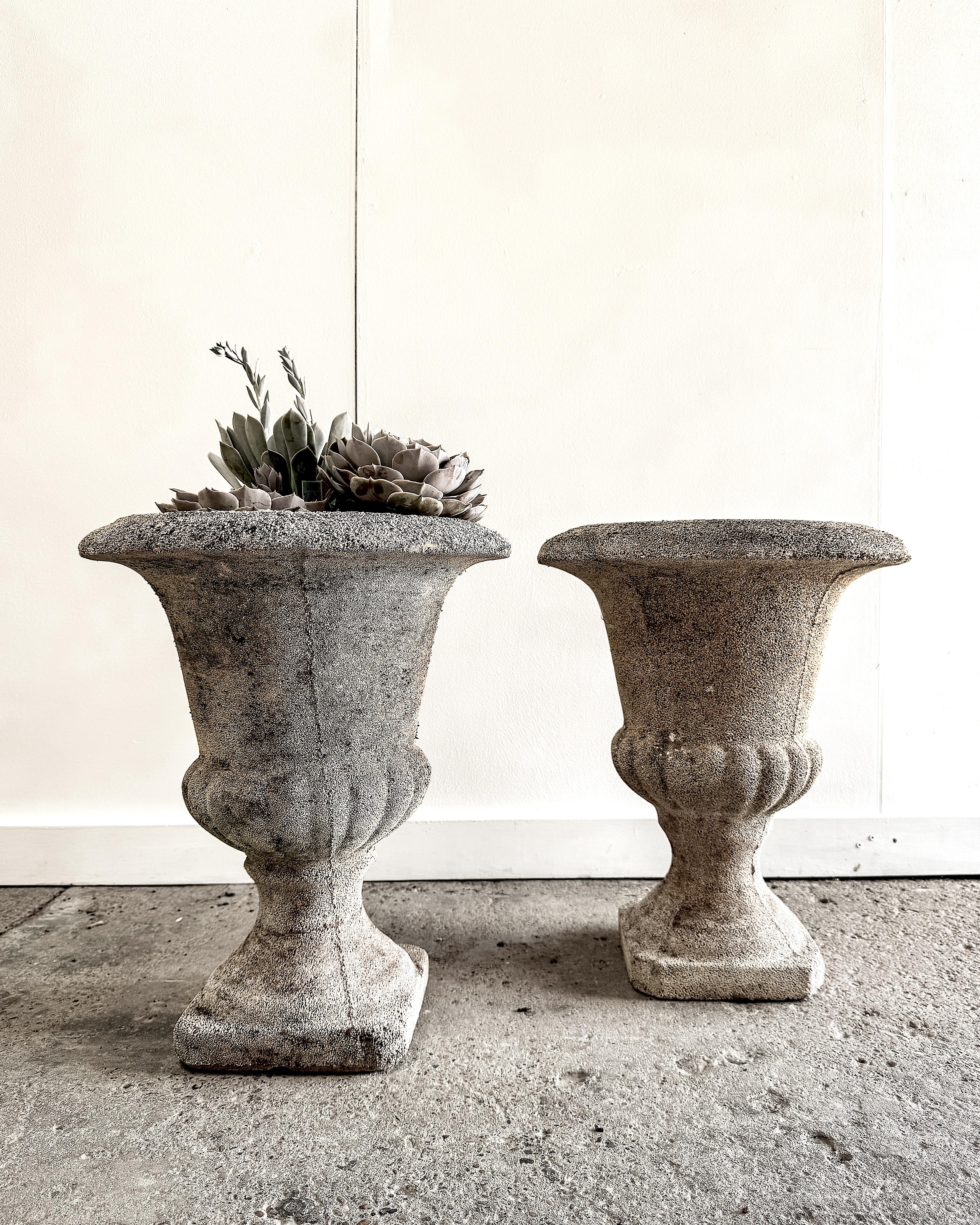 A classic pair of French urns that lends timeless form and texture to the garden or patio. Crafted from a cement composite with visible aggregate, they feature a gently weathered surface that speaks to decades spent outdoors. 

The elegant