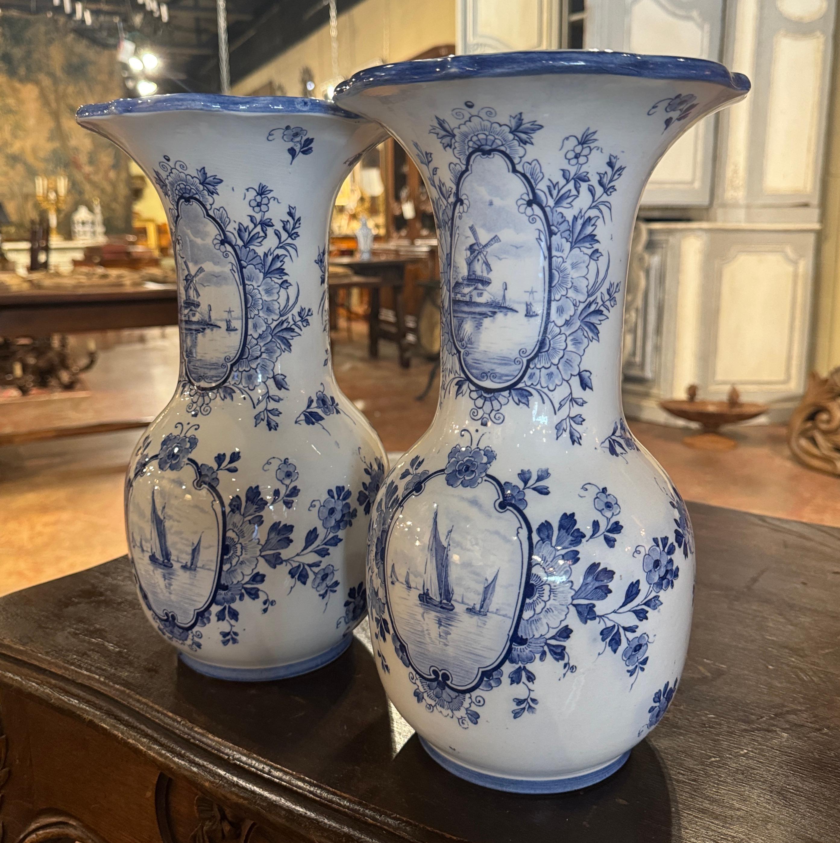 Décorez une étagère ou une table console avec cette élégante paire de vases anciens de Delft. Fabriqués en Hollande vers 1920, les deux vases à large ouverture présentent un bord festonné au sommet, un long col et un fond de forme ronde. Chaque