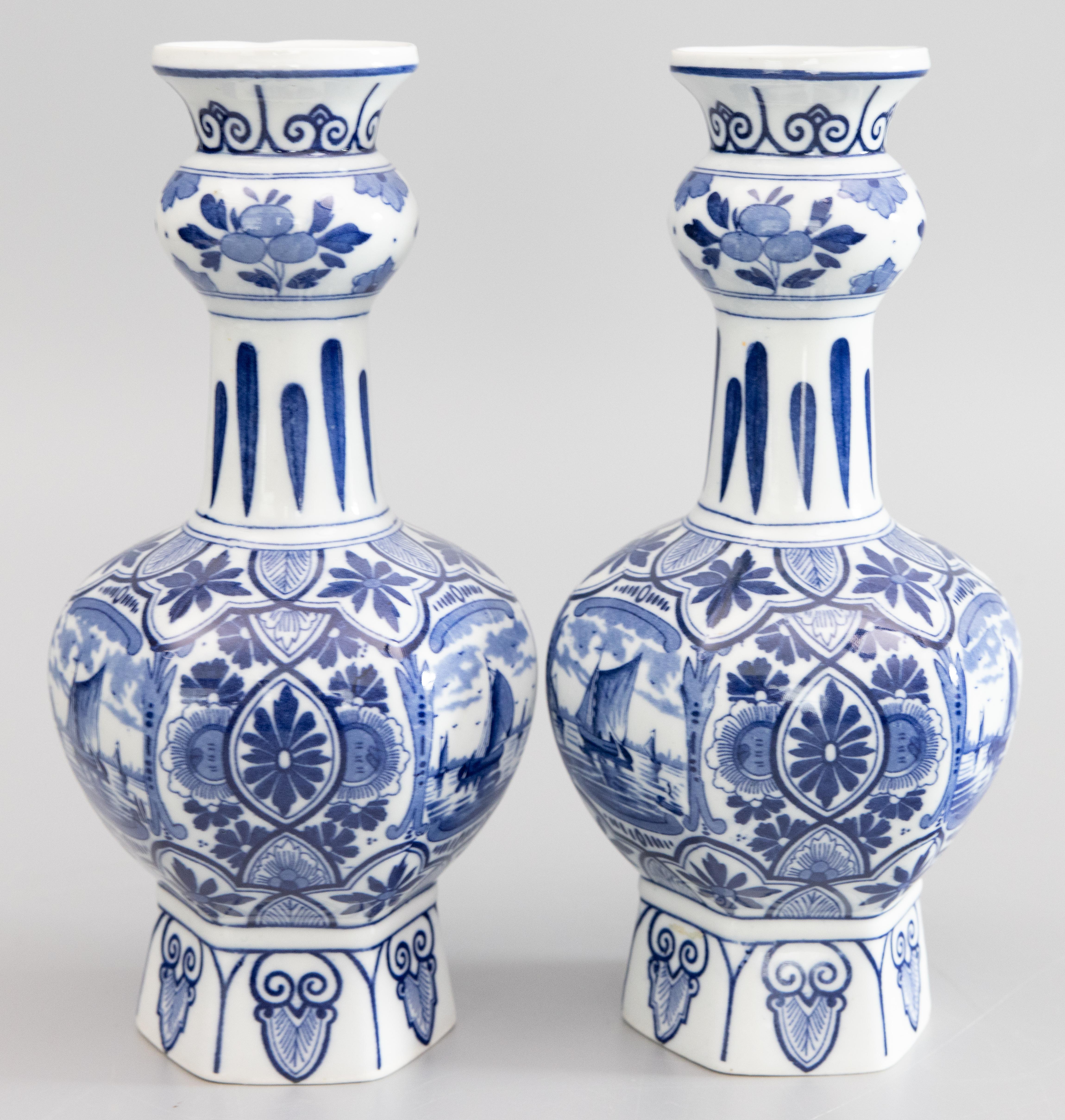 A lovely pair of antique early 20th-Century Dutch Delft faience knobble garlic mouth vases with a hexagonal shape. Maker's mark on reverse. These beautiful vases are hand molded and hand painted with vibrant cobalt blue and white sailboat, windmill,