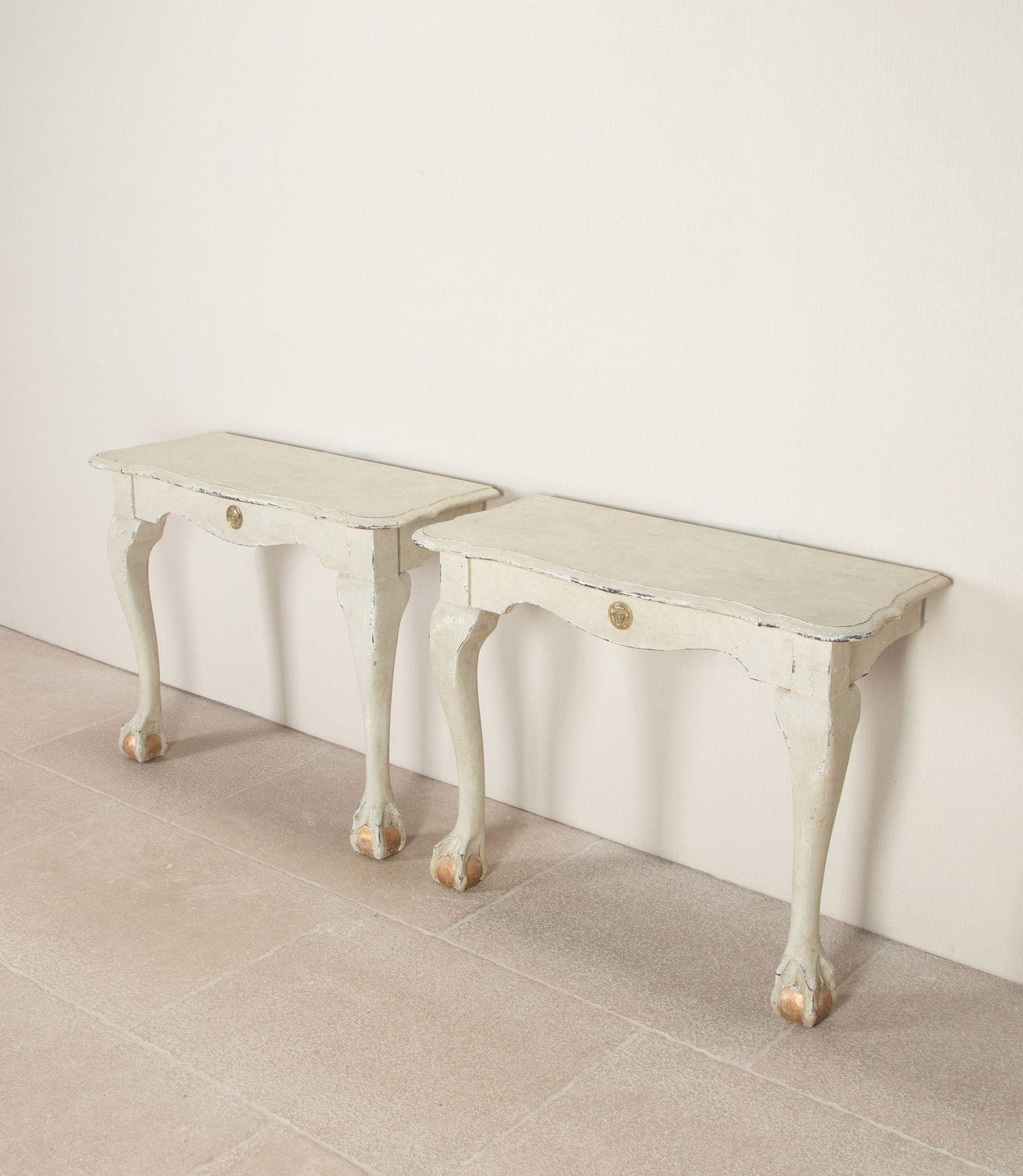 A pair of early 20th Century Dutch painted wall hanging console tables.Of serpentine form standing on cabriole legs with lion paw and sphere feet. The frieze, with a bronze classical mount finished in stone grey paint with remnants of gilding to the