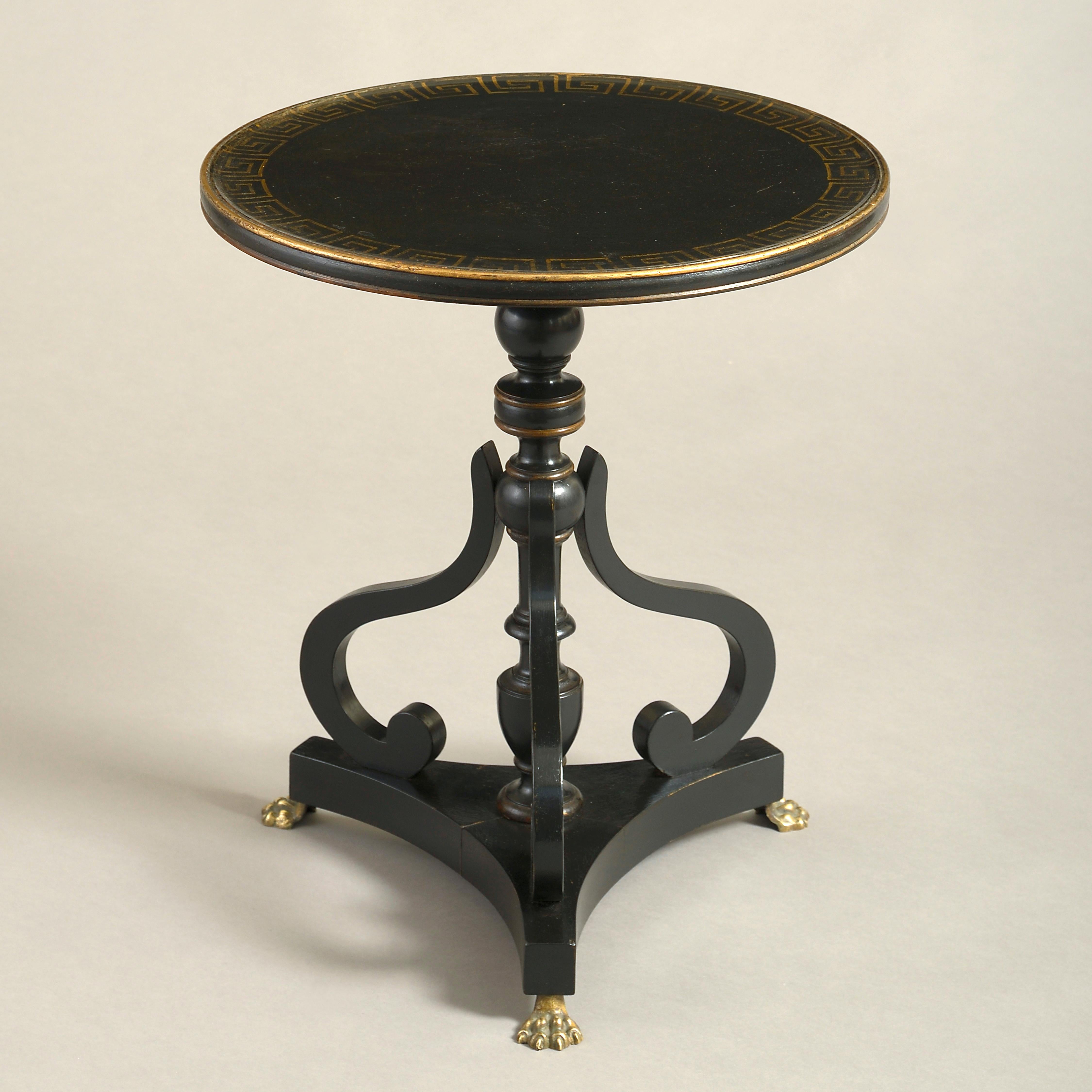 A pair of early 20th century ebonized end tables in the Regency taste, each having a circular dish top with gilded Greek key decoration, upon a turned stem with scrolling supports, set upon a triform concave plinth and terminating in brass paw feet.