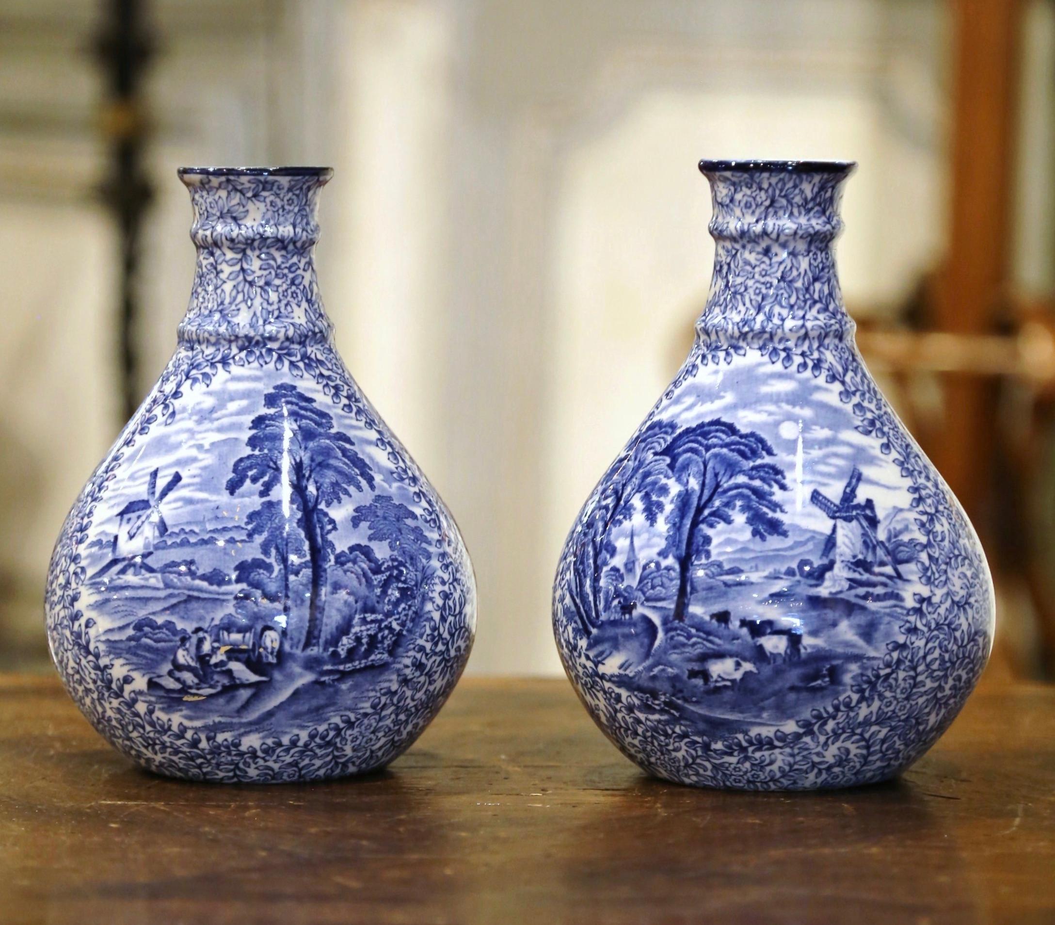 Decorate a shelf or console table with this elegant pair of antique Delft style vases. Crafted in England circa 1920, the vases are round in shape over an elegant neck. Each vessel is hand painted in the blue and white Delft palette, and each