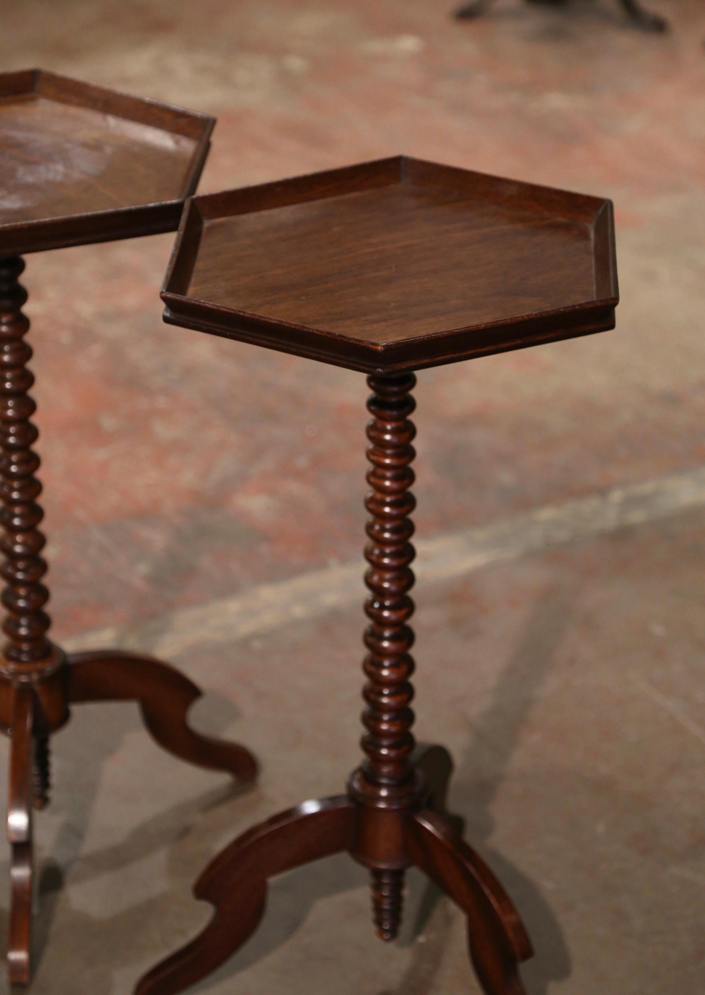 Decorate a living room or den with this elegant pair of antique occasional  tables. Crafted in England circa 1920, each fruit wood end table stands on a tripod base ending with three legs over a carved turned stem. The surface is dressed with a