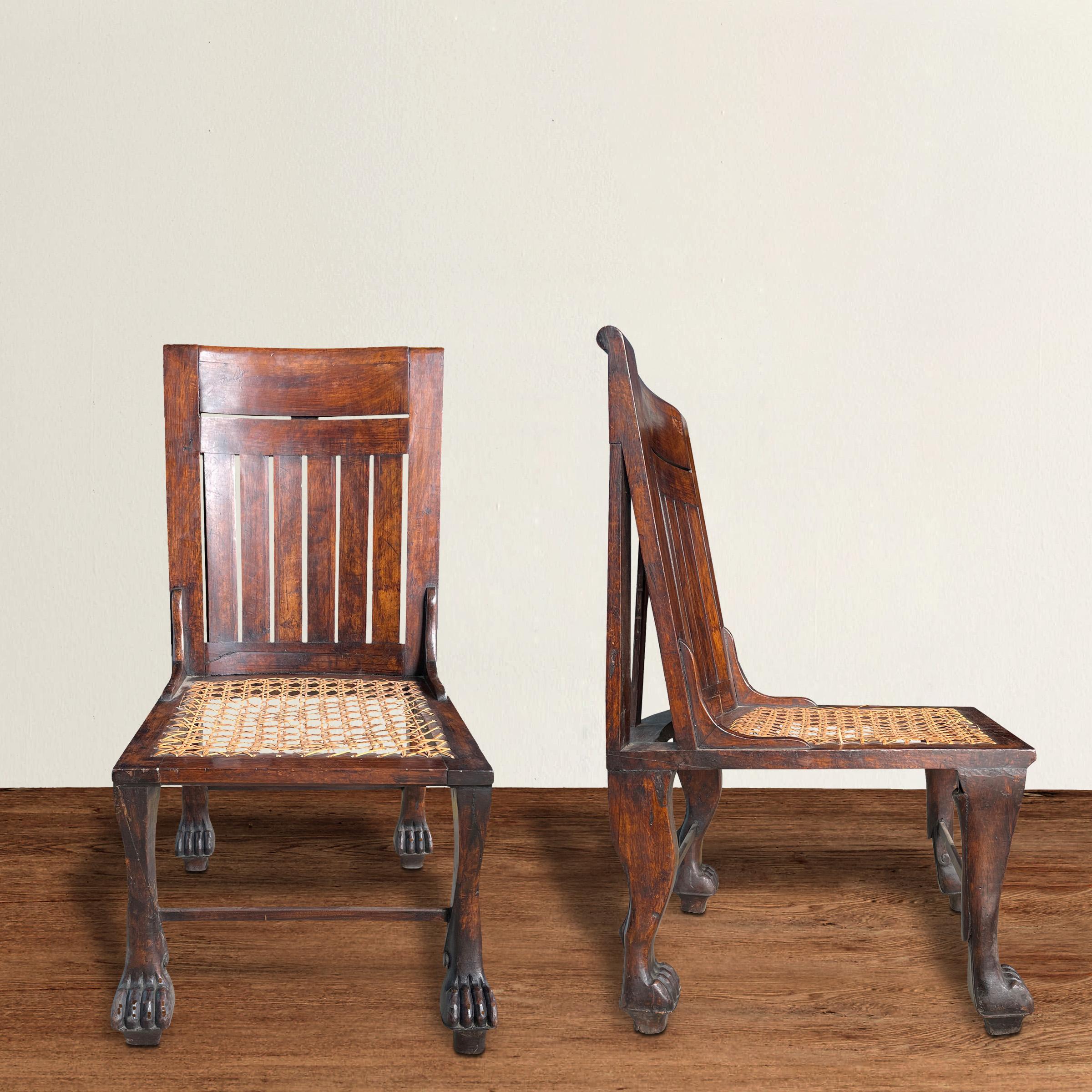 A striking and rare pair of early 20th century English Egyptian Revival chairs inspired by an 18th Dynasty chair discovered in 1905. The frames are carved of walnut and feature legs carved to imitate the fore and hind legs of lions, and with caned