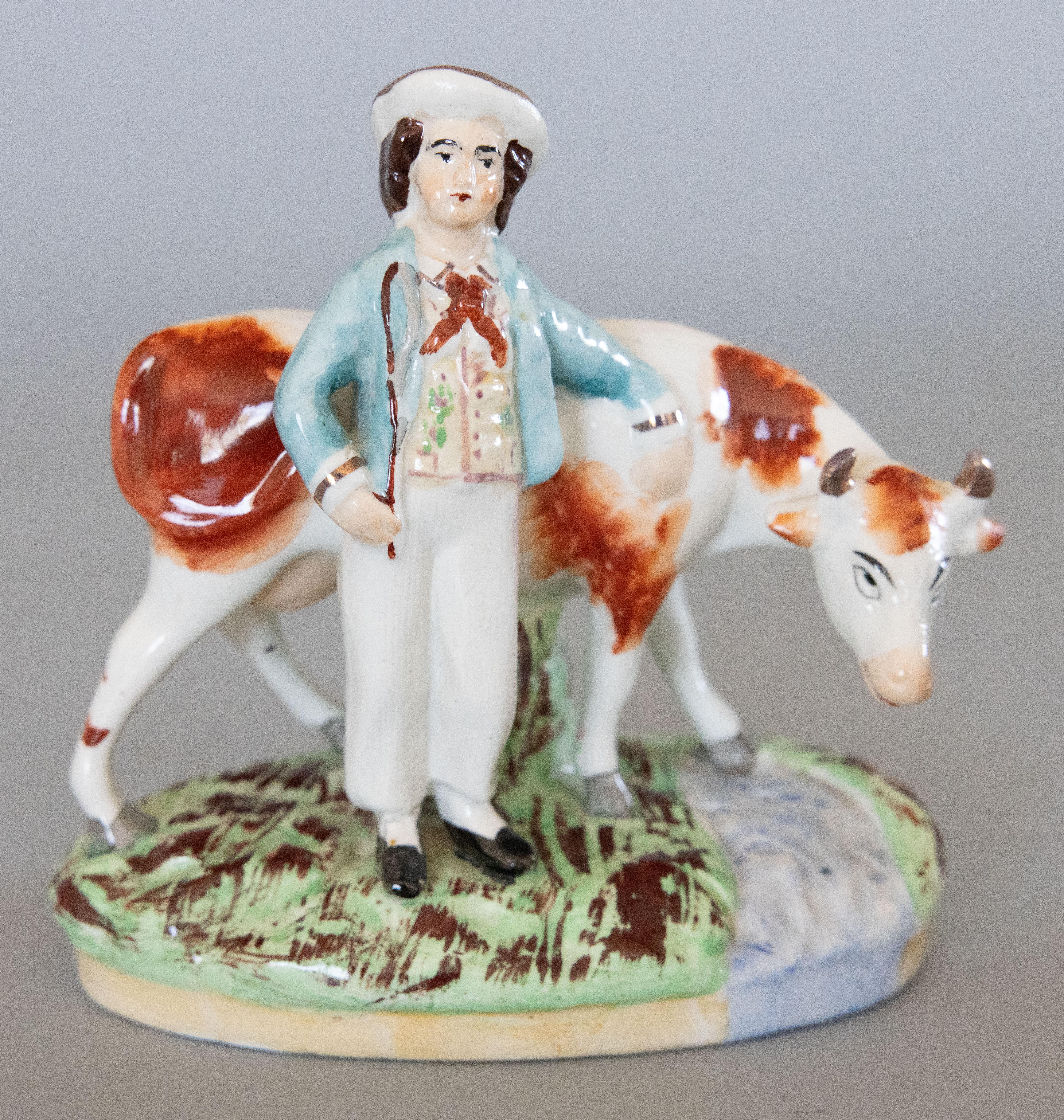 A superb pair of antique early 20th Century English Staffordshire boy and girl cow figurines. Maker's mark on reverse. These charming figurines feature a finely hand painted lad and milk maid with their arms resting on red and white cows standing on
