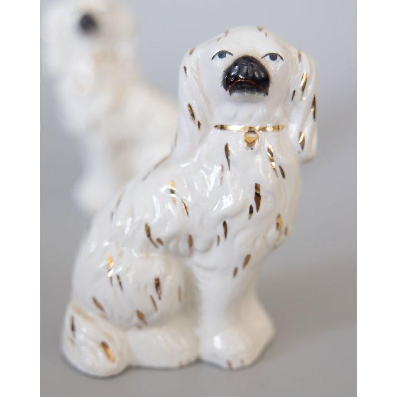 A wonderful pair of early 20th-Century English Staffordshire spaniel dogs with gilt accents. Maker's mark on reverse. These charming dogs are hand painted with beautiful details and the sweetest expressions. It's hard not to be smitten! They are in