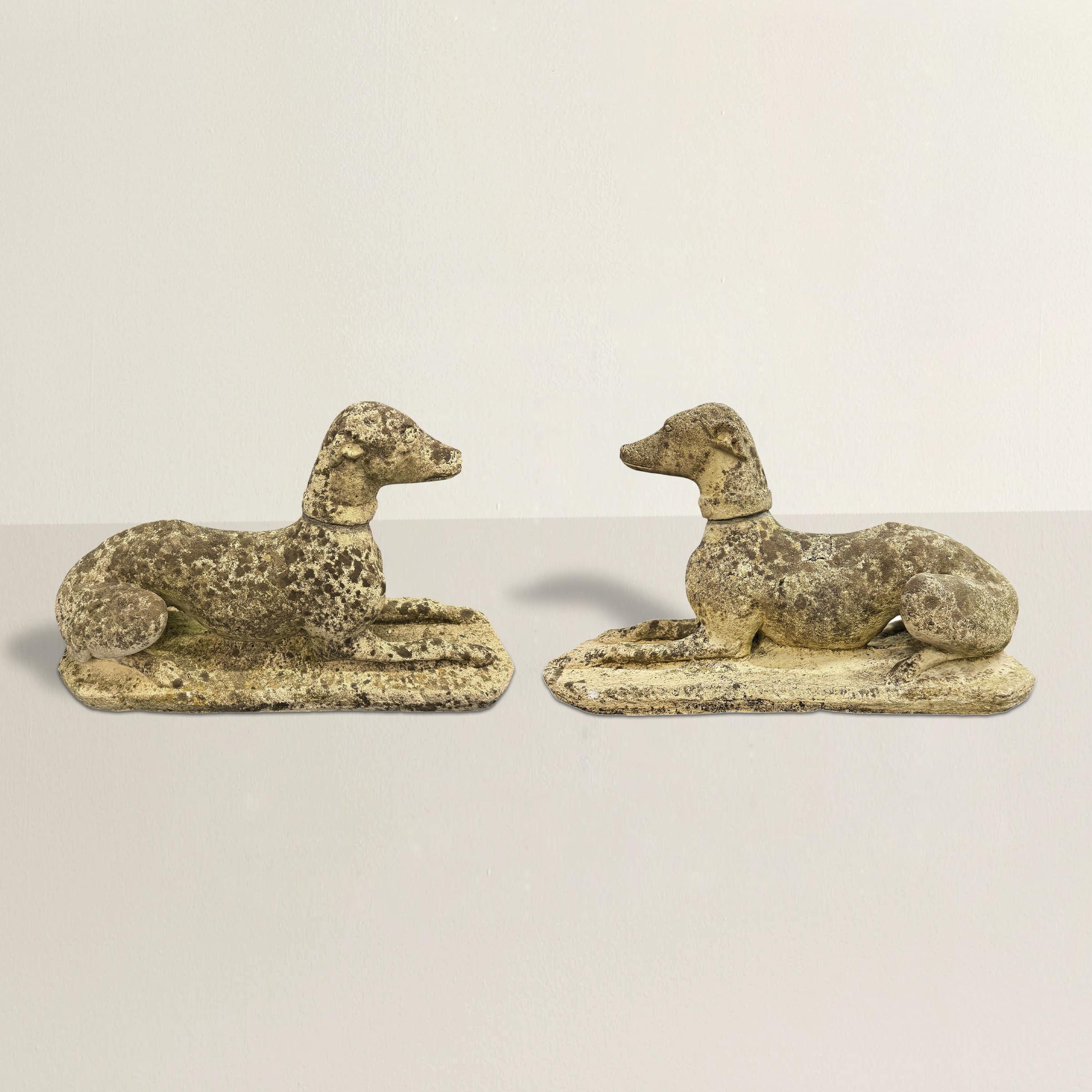 This pair of early 20th-century English cast stone whippets exudes timeless charm and quiet elegance. Each whippet is depicted in a graceful resting position, with front legs outstretched and back legs tucked neatly to the side, heads facing forward