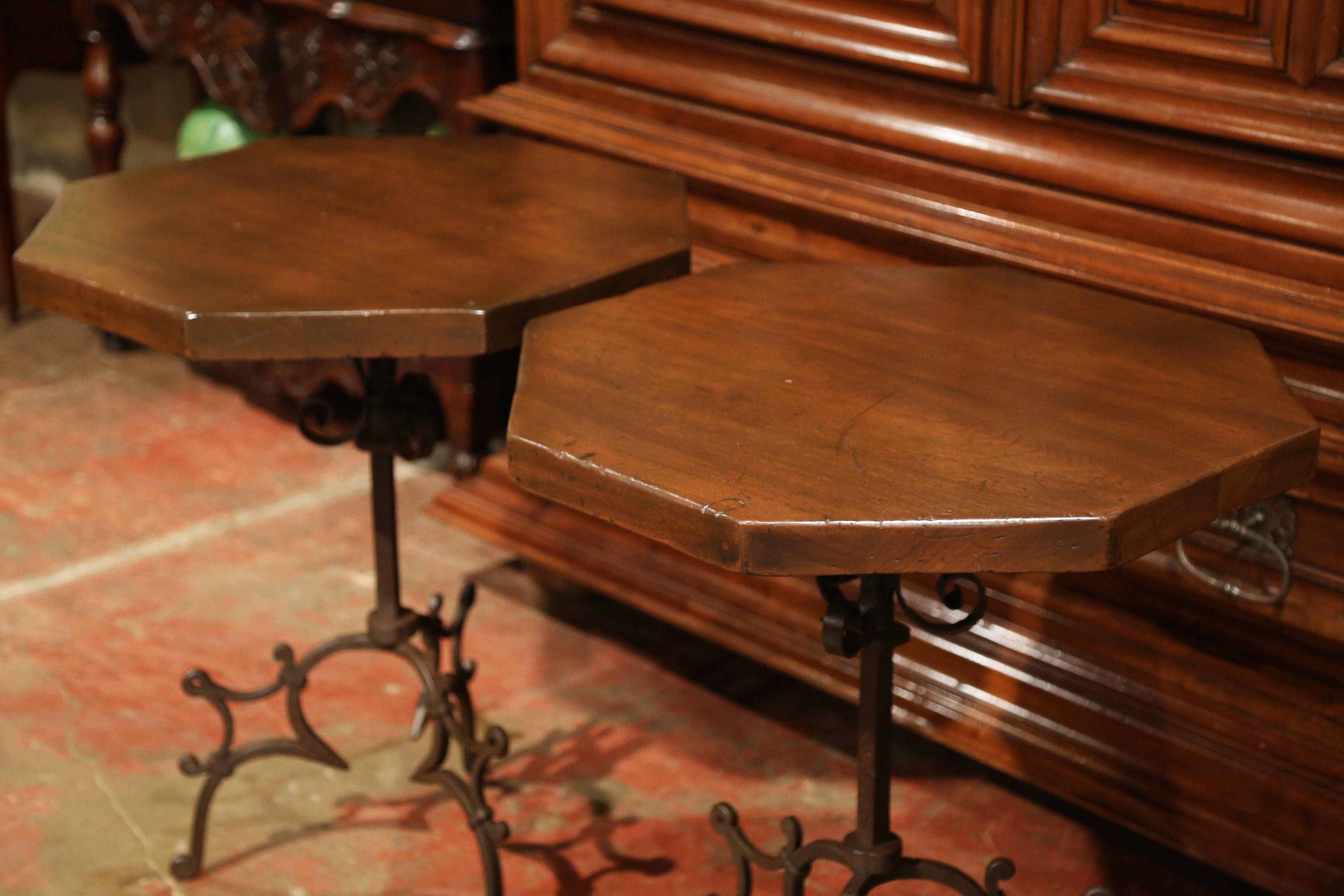Place this pair of Gothic style side tables on either side of a sofa as end tables or as bedside tables, crafted in Spain circa 1920, each table stands on a three-leg wrought iron base with scroll decor, and features a fruitwood octagonal top. Both