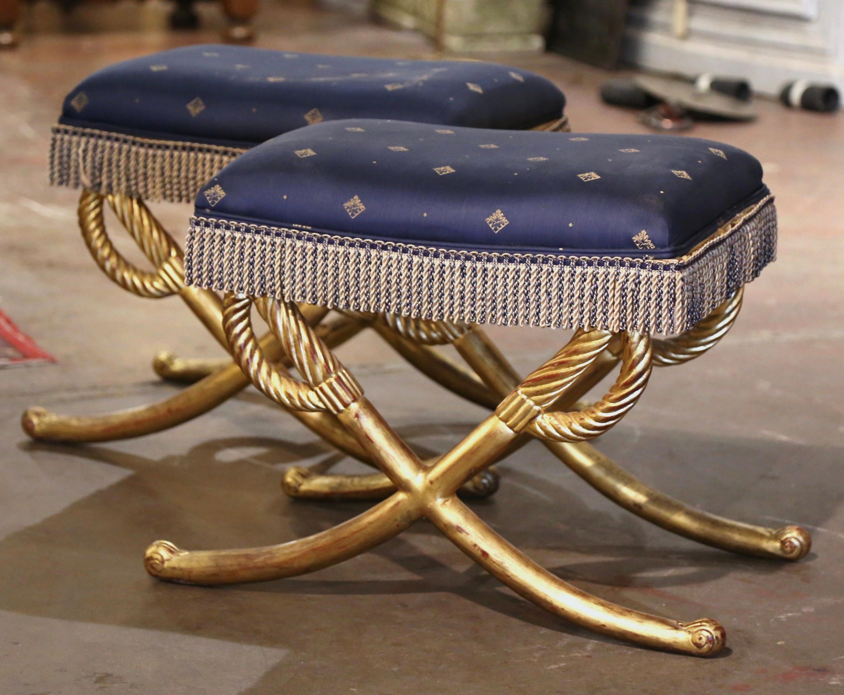 Embellish your formal living room with this elegant pair of antique curule stools. Crafted in France circa 1920, these stools feature an ornate carved base decorated with two hand carved crossed swords ending with scroll leaf feet. The seats are