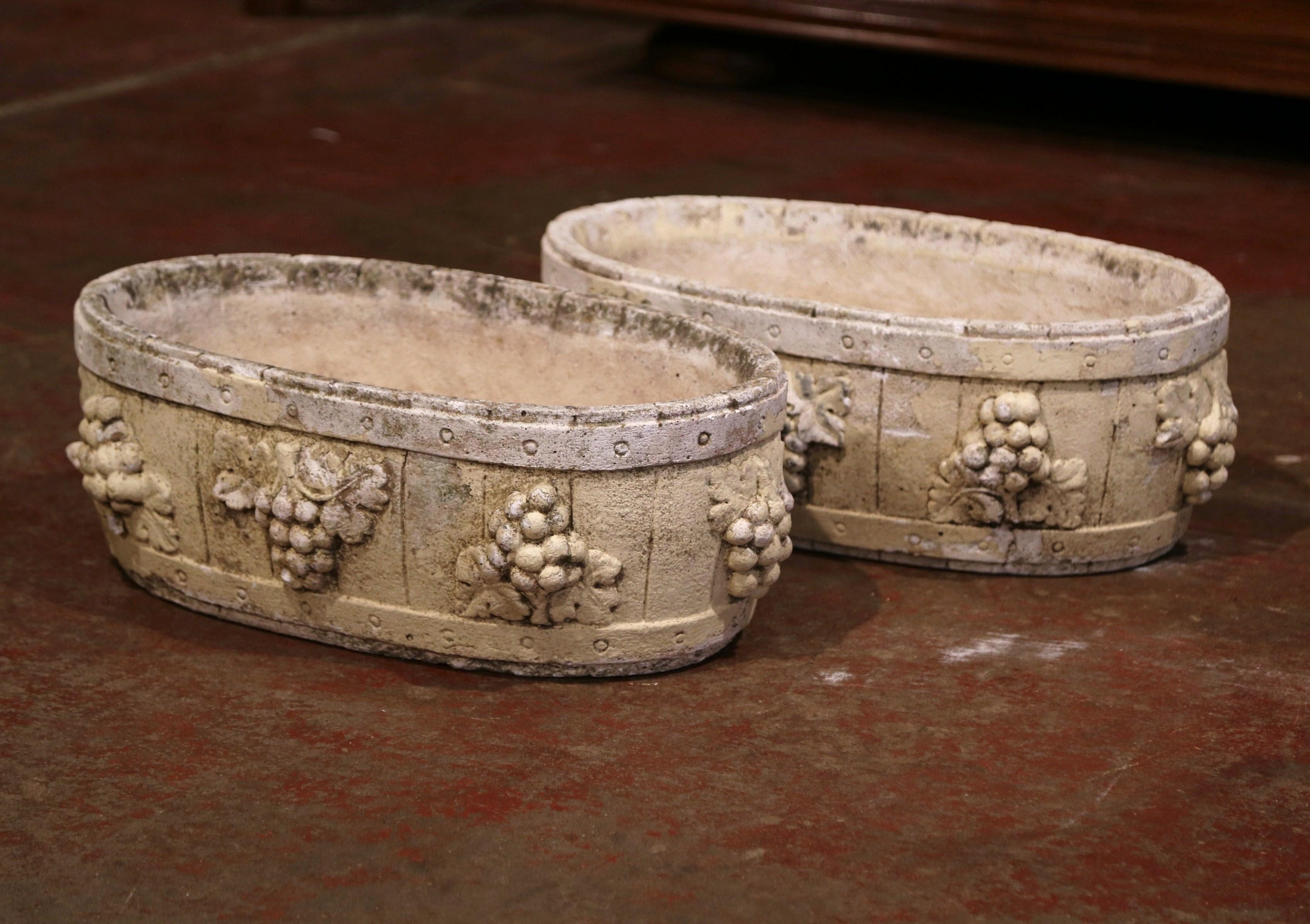 Decorate a patio with this pair of weathered outdoor planters. Carved in Normandy France, circa 1930, each oval antique jardinière with drainage holes in the bottom, is decorated with hand carved high relief bunch of grape and leaf decor all around.