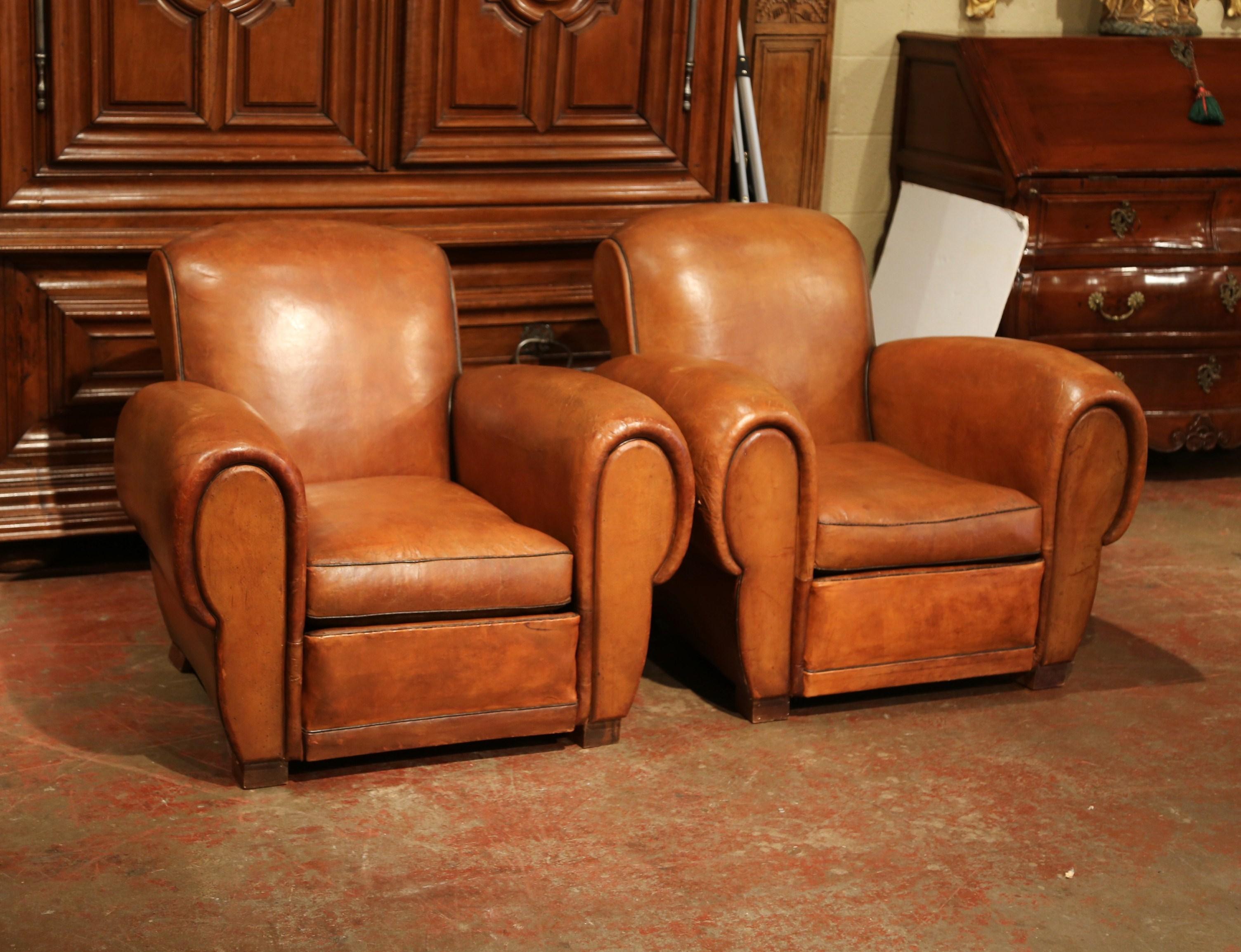 These antique Art Deco club chairs were crafted in France, circa 1920. The stately chairs feature wide, rounded armrests, a pitch back with a curved shape at the top, and square wooden feet at the base. The comfortable armchairs are in very good
