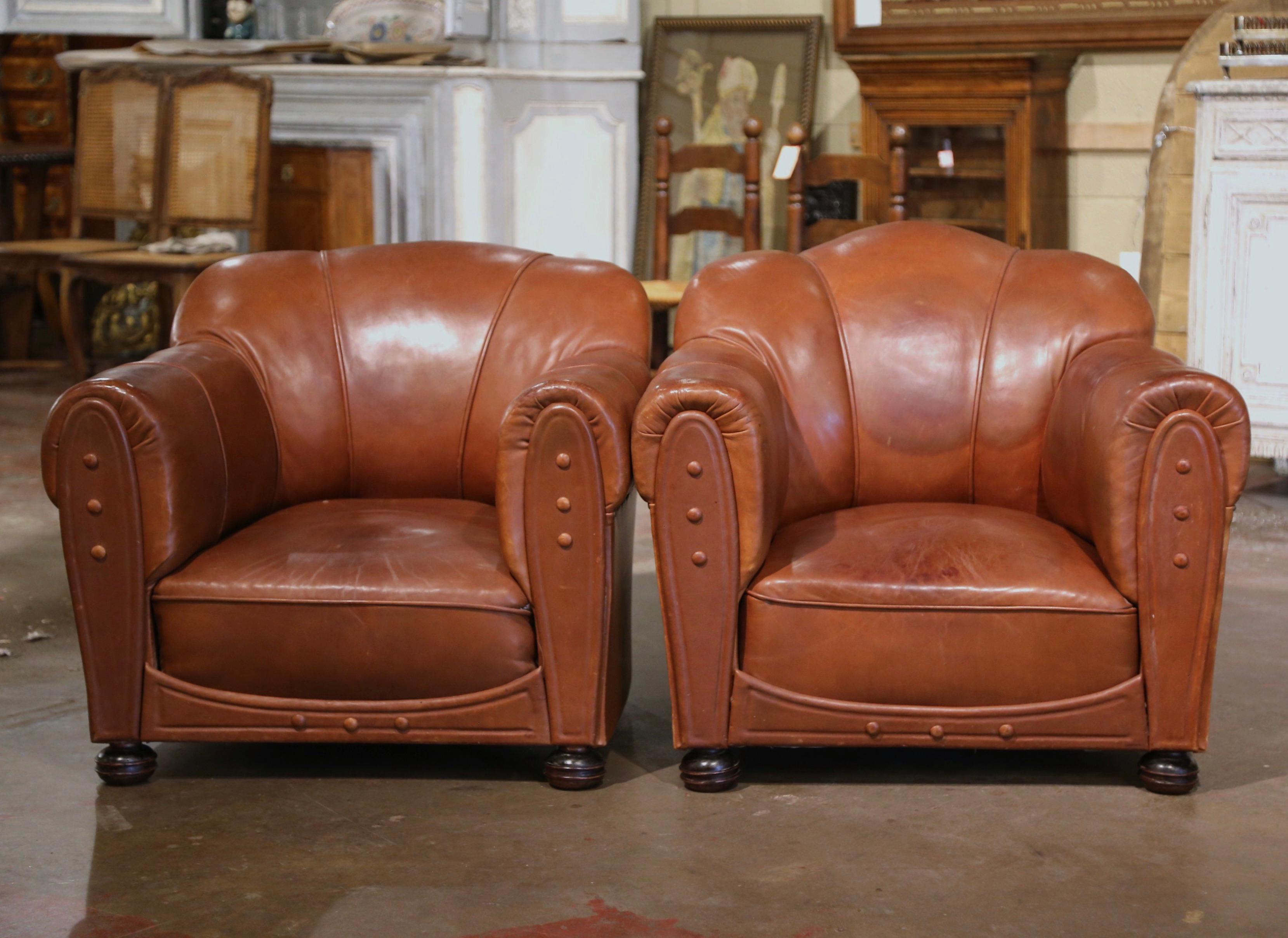 These cozy, antique Art Deco club chairs were crafted in France, circa 1930. The stately, masculine chairs feature wide, rounded armrests, an arched and scalloped top shape back, and round wooden feet in the front and square feet in the back. The