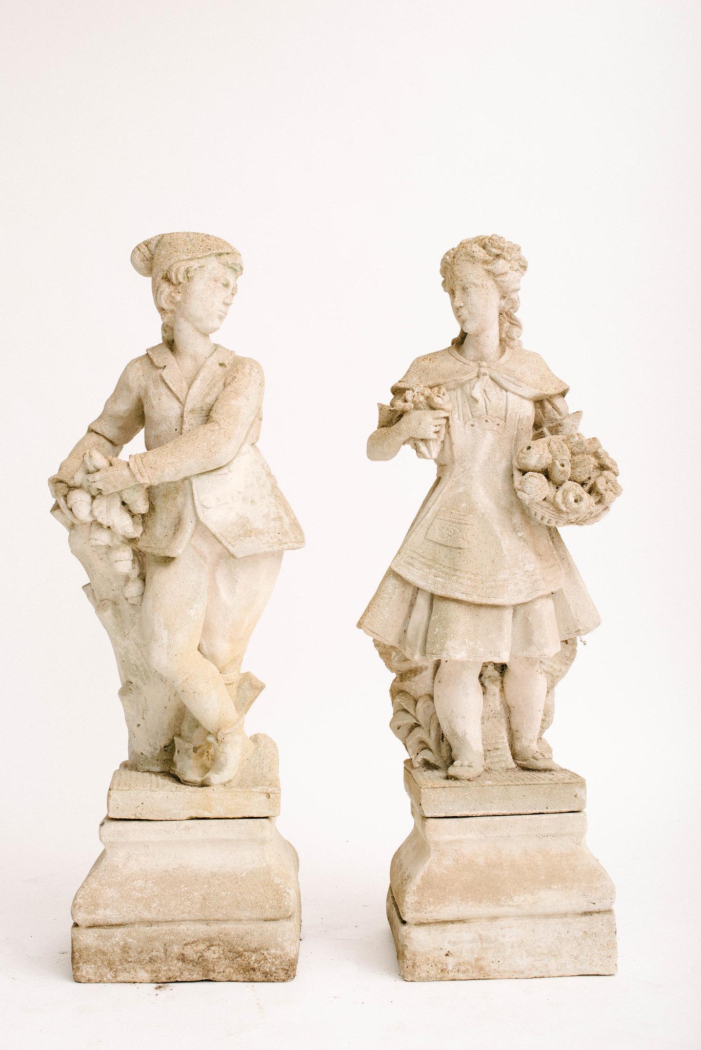 A lovely pair of 20th century concrete garden figures from France. He is perched next to an oak stump with foliage and acorns in hand. She carries two floral bouquets. These figures both sit atop two separate pedestal bases.