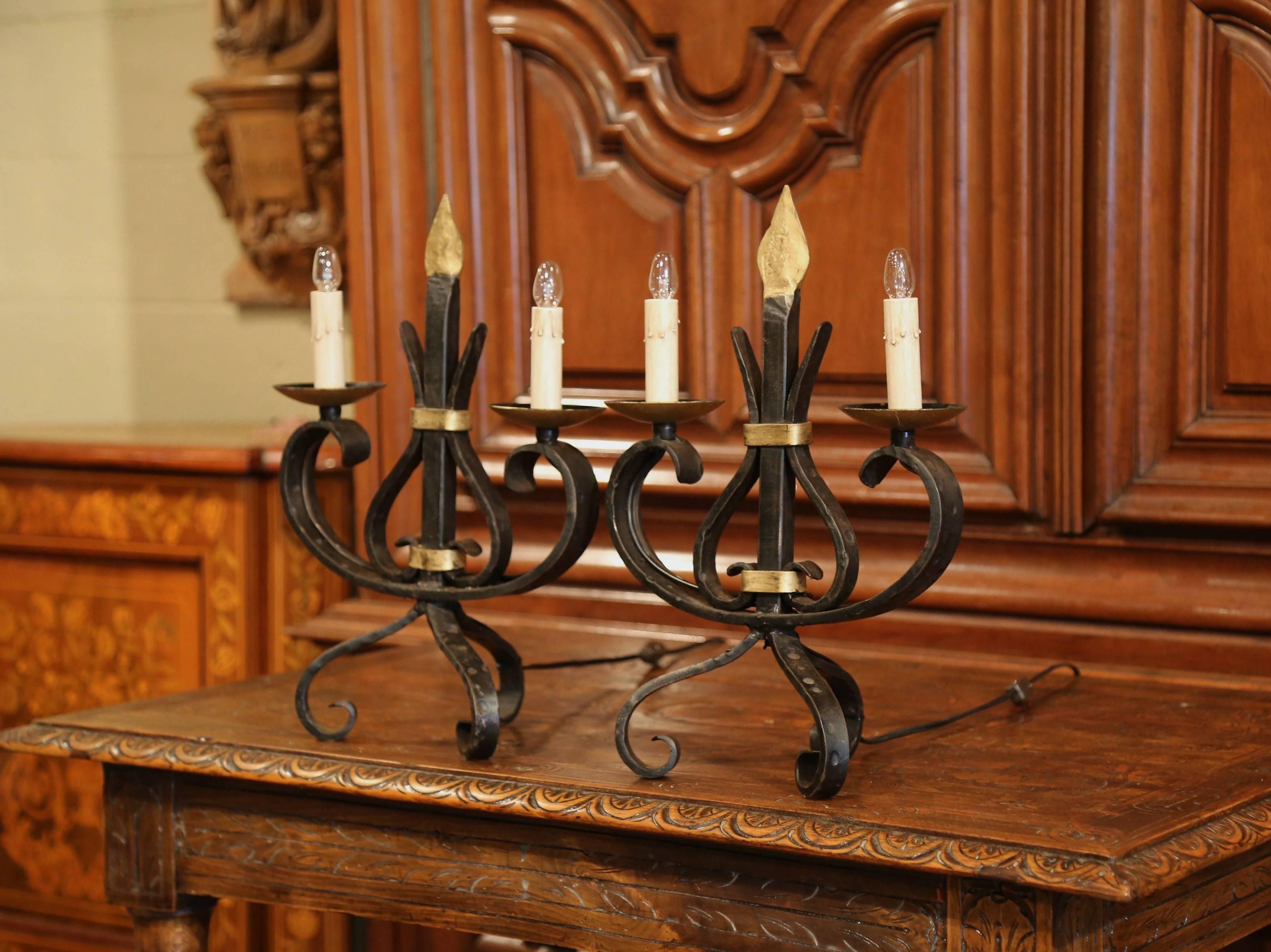 Elegant pair of antique Gothic candelabras from Southern France, crafted circa 1920, the forged fixtures Stand on three curved legs, they have two lights newly wired with ornate iron work in the center. The free standing table lamps are in excellent