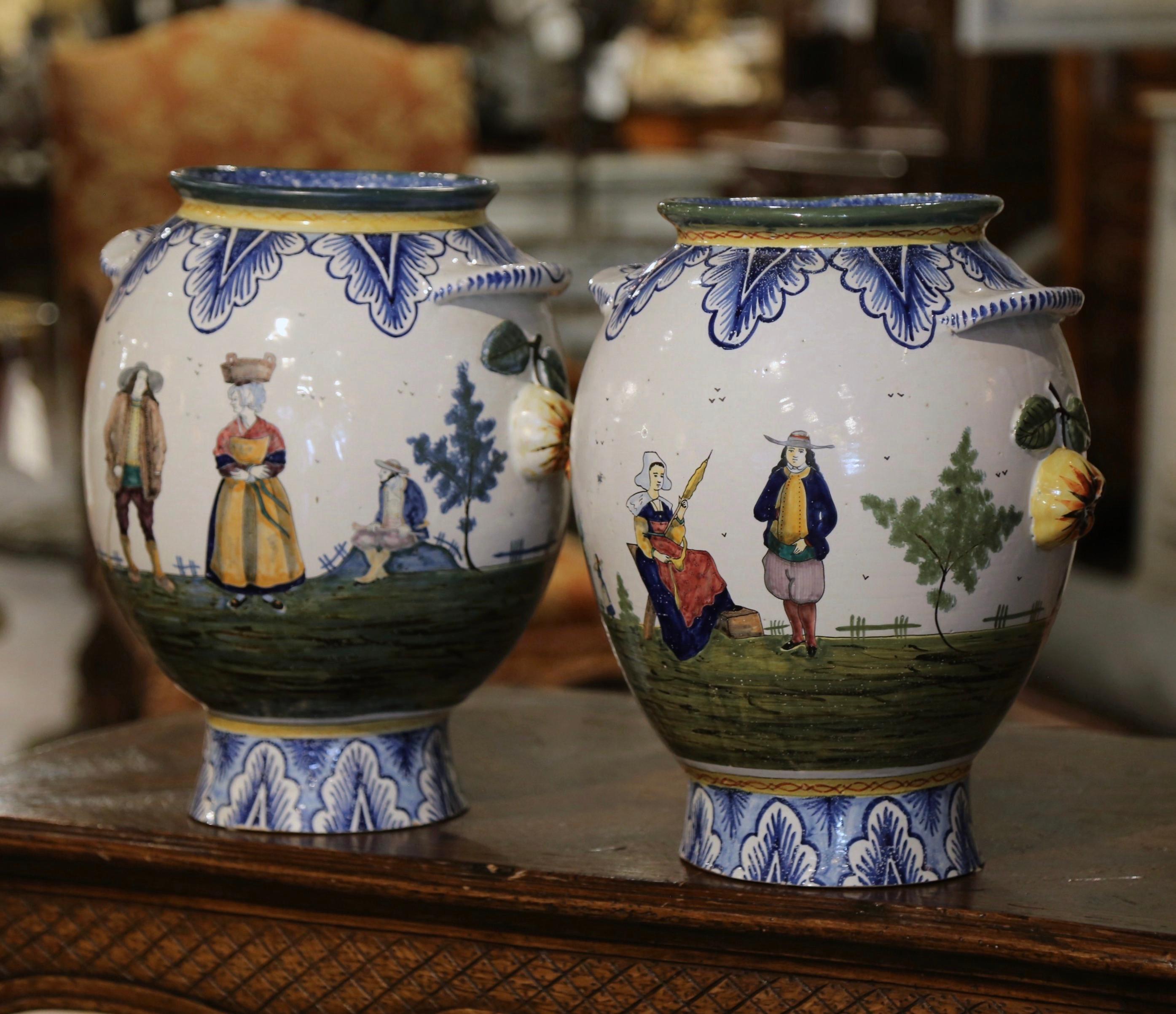 Decorate a mantel or table with this colorful pair of antique faience vases. Crafted in Brittany, France, circa 1920, each large planter is round in shape, and dressed with small side handles; it is further embellished with fruit and leaf motifs in