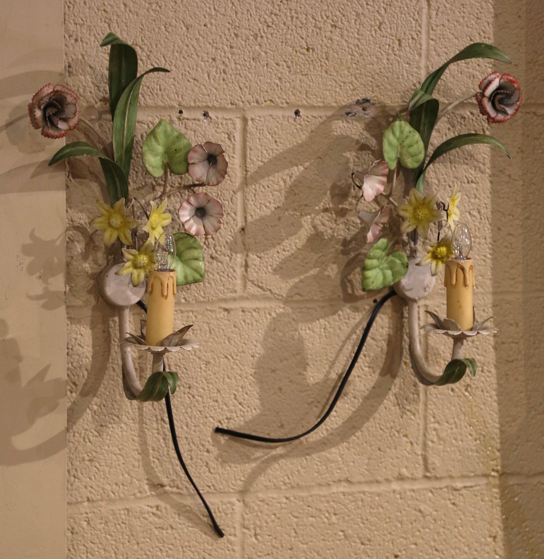 This elegant pair of antique sconces was created in France, circa 1920. The feminine wall fixtures are decorated with hand-painted pink petunia and yellow daffodil flowers, accented with a variety of green leaves. Each colorful wall light has one