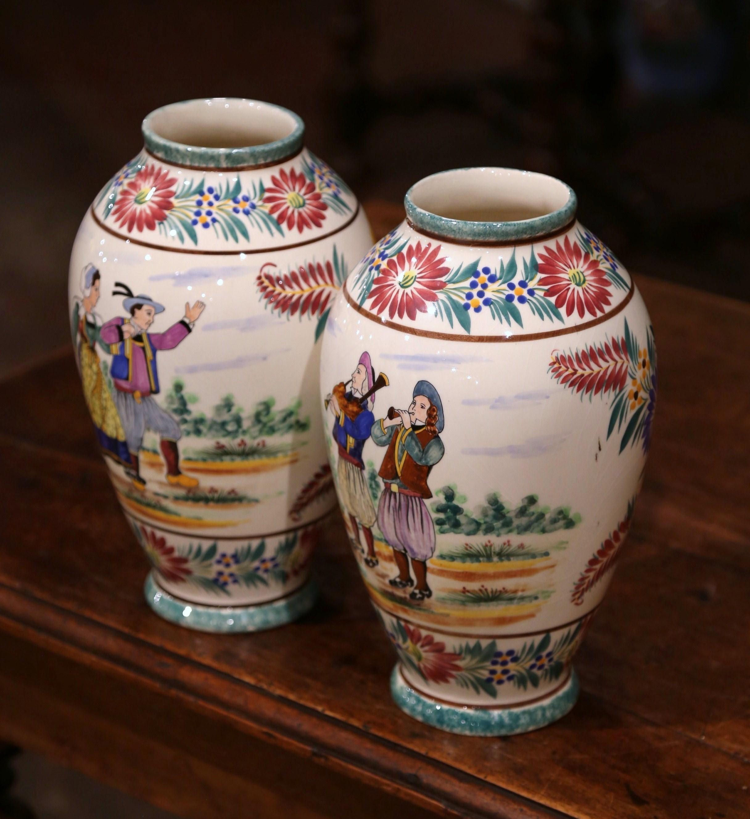 Decorate a mantel or table with this colorful pair of antique faience vessels. Crafted in Brittany, France, circa 1930, both hand painted vases are round in shape, and depict Britons people dressed in traditional outfits. One vase features a couple