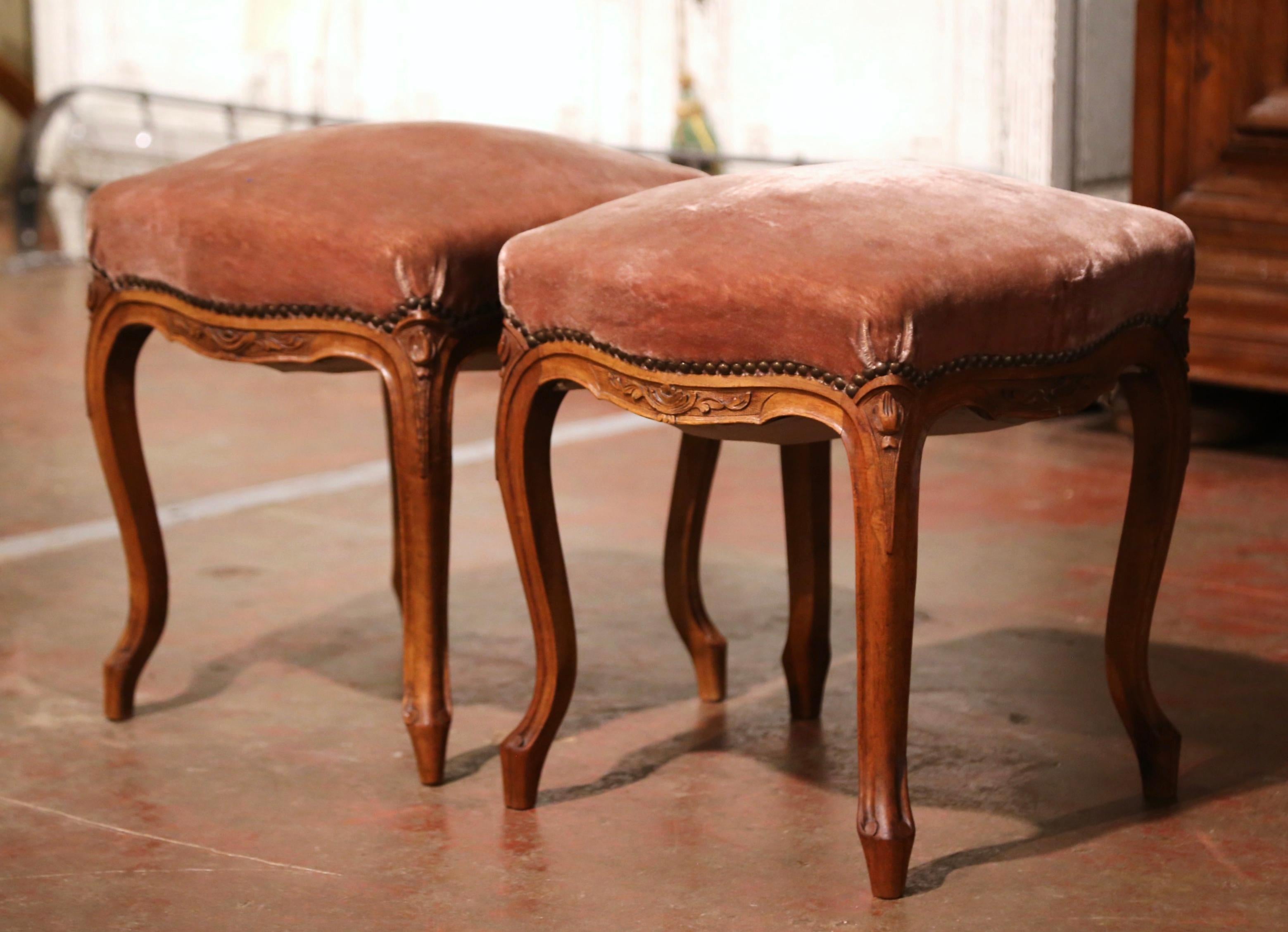 These elegant antique stools were crafted in Provence, France circa 1920. Standing on cabriole legs ending with scrolled feet and decorated with carved leaf decor at the shoulder, each stool features a bombe scalloped apron with foliage motifs. Each