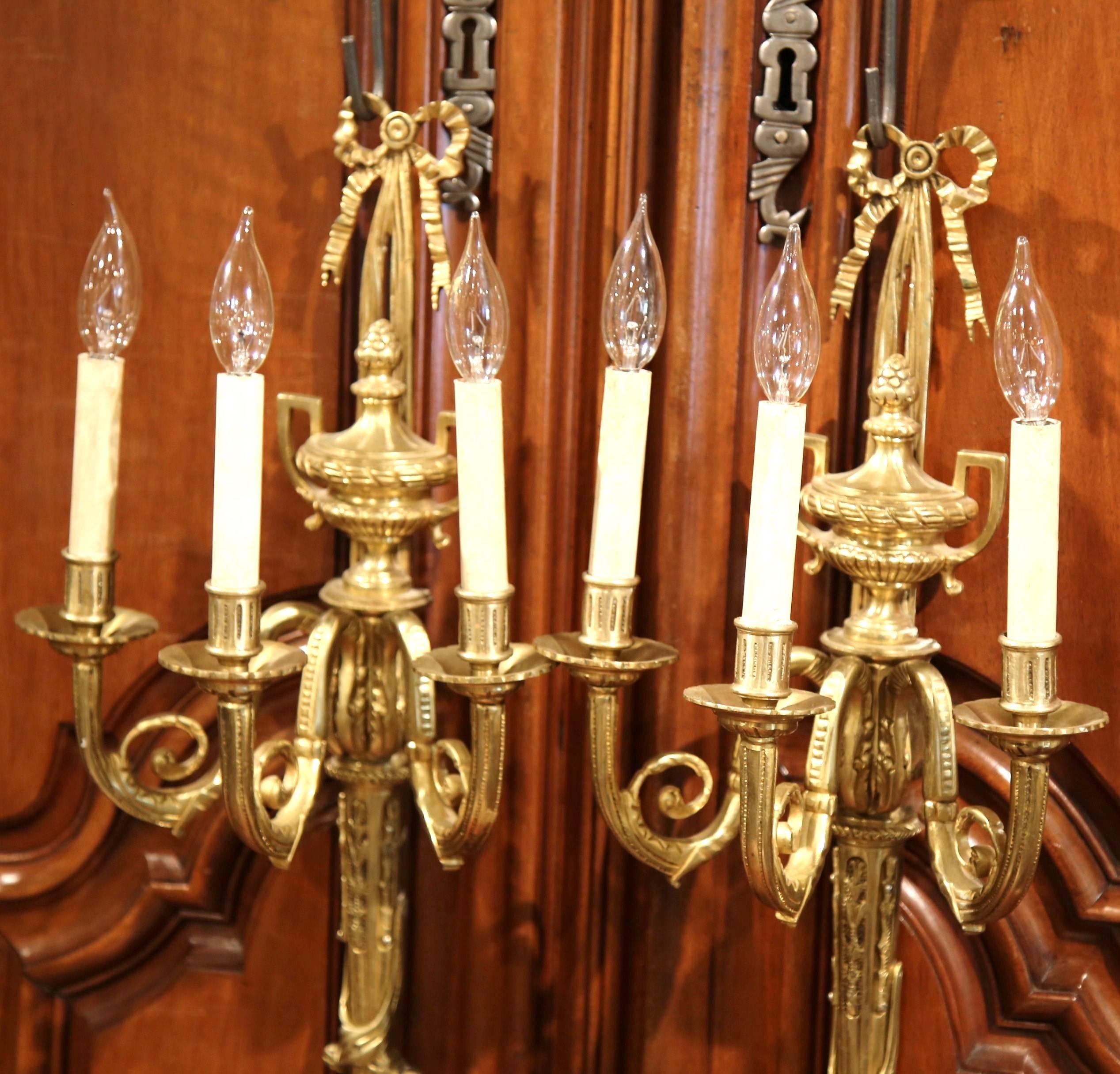 These large and elegant antique bronze sconces were crafted in France, circa 1920. Each wall sconce has three-light newly wired, and features a traditional Louis XVI ribbon bow and a classical vase decor underneath. The delicate, traditional light