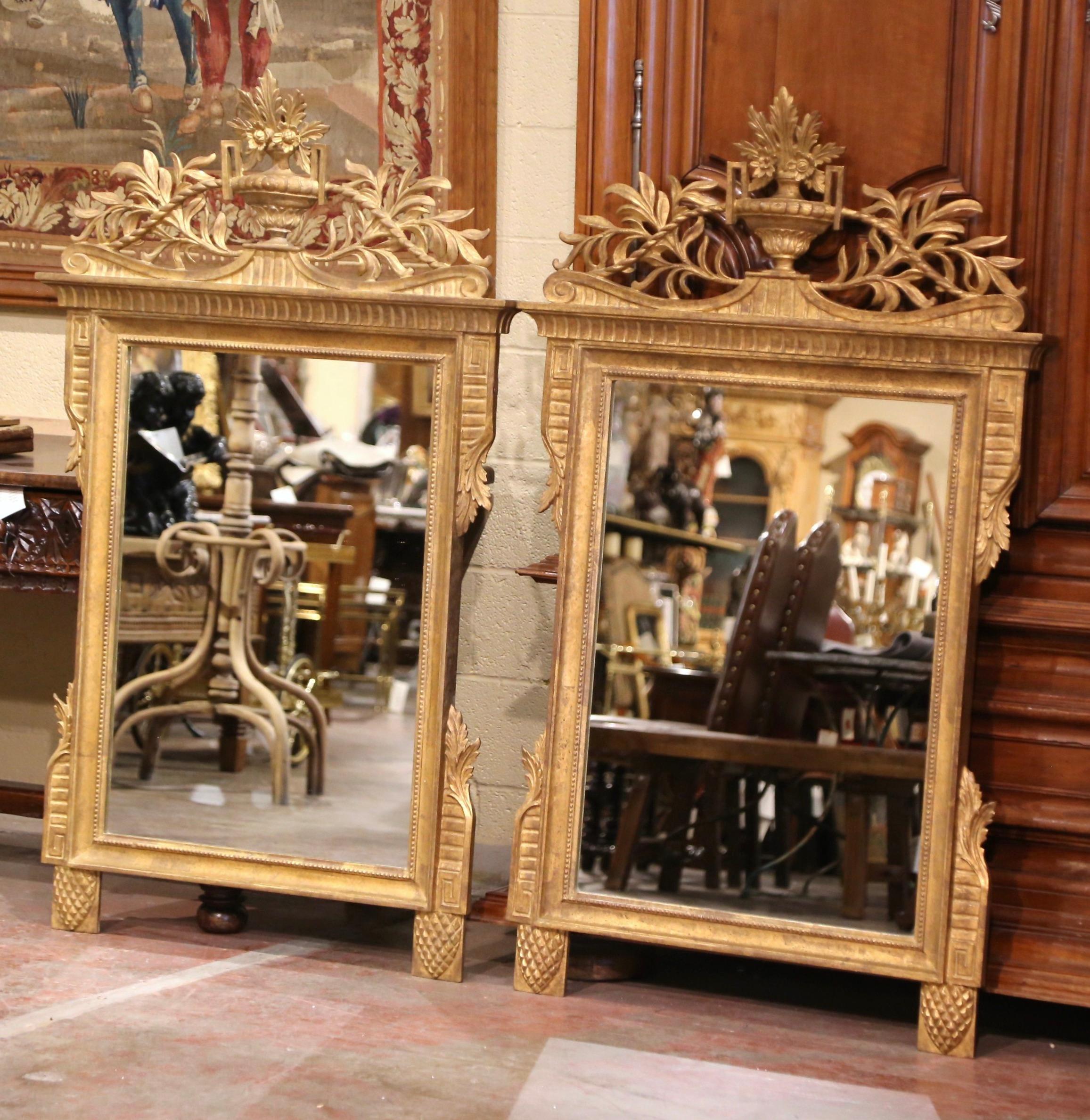 Decorate a living room with this elegant pair of almost 5 foot tall antique wall mirrors. Hand carved in France circa 1930 and rectangular in shape, each large mirror is decorated with the traditional Louis XVI flower vase at the pediment and