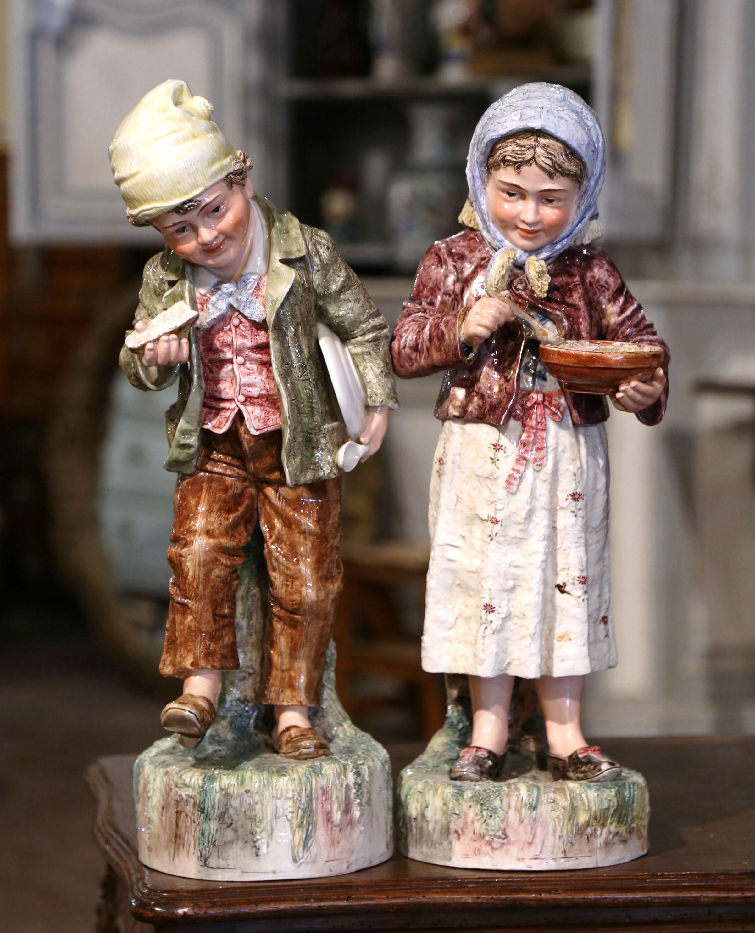 Decorate a kitchen counter or a study with this colorful pair of antique barbotine sculptures. Crafted in France circa 1920 and built of porcelain, the tall figurines are standing on a circular base, and depict two cheerful and jovial children