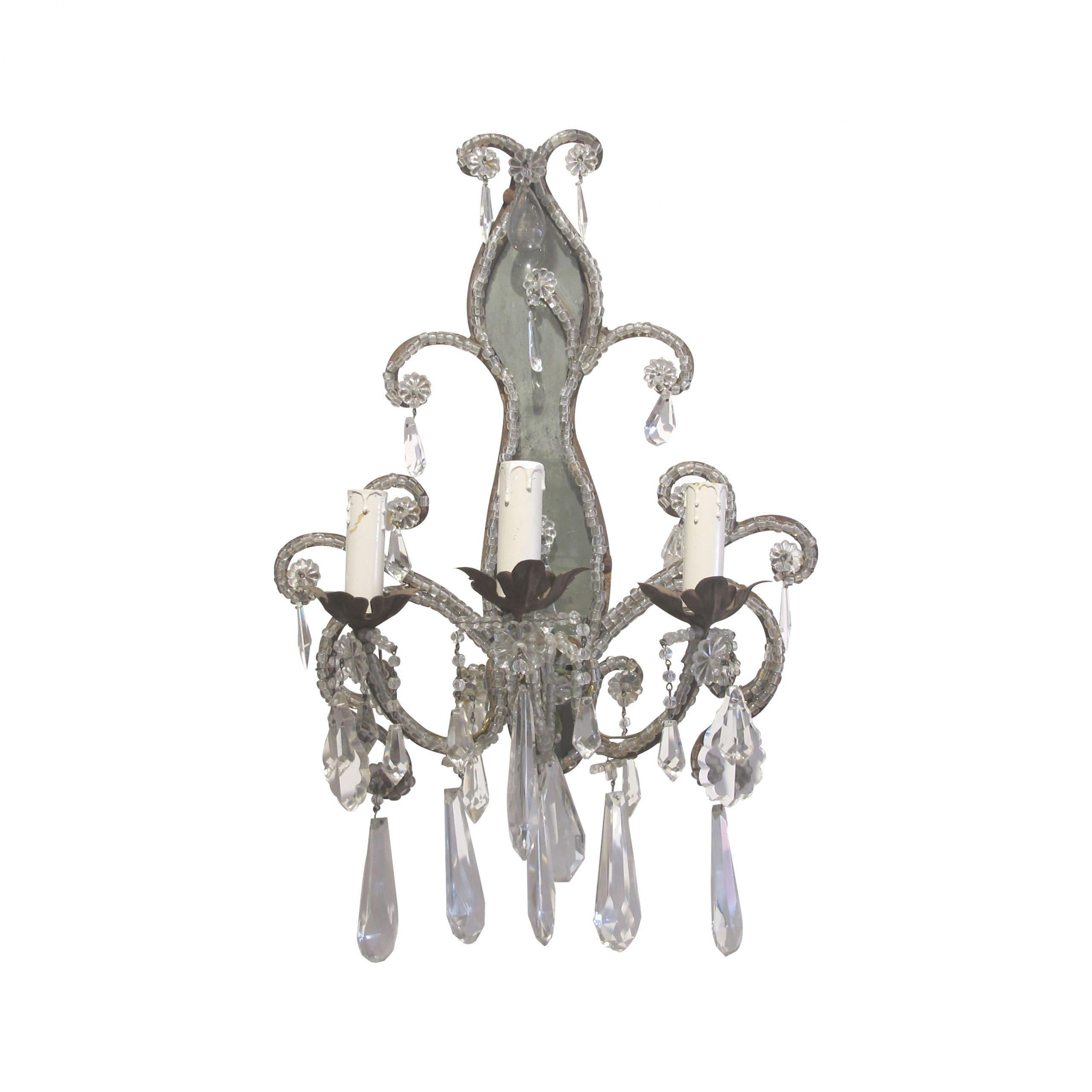 An elegant pair of early 20th century French wall lights with crystal bead swags and pampilles. Each wall sconce has three separate arms each featuring a candle shaped bulb holder at the end of each one. One sconce's mirrored backplate has a crack