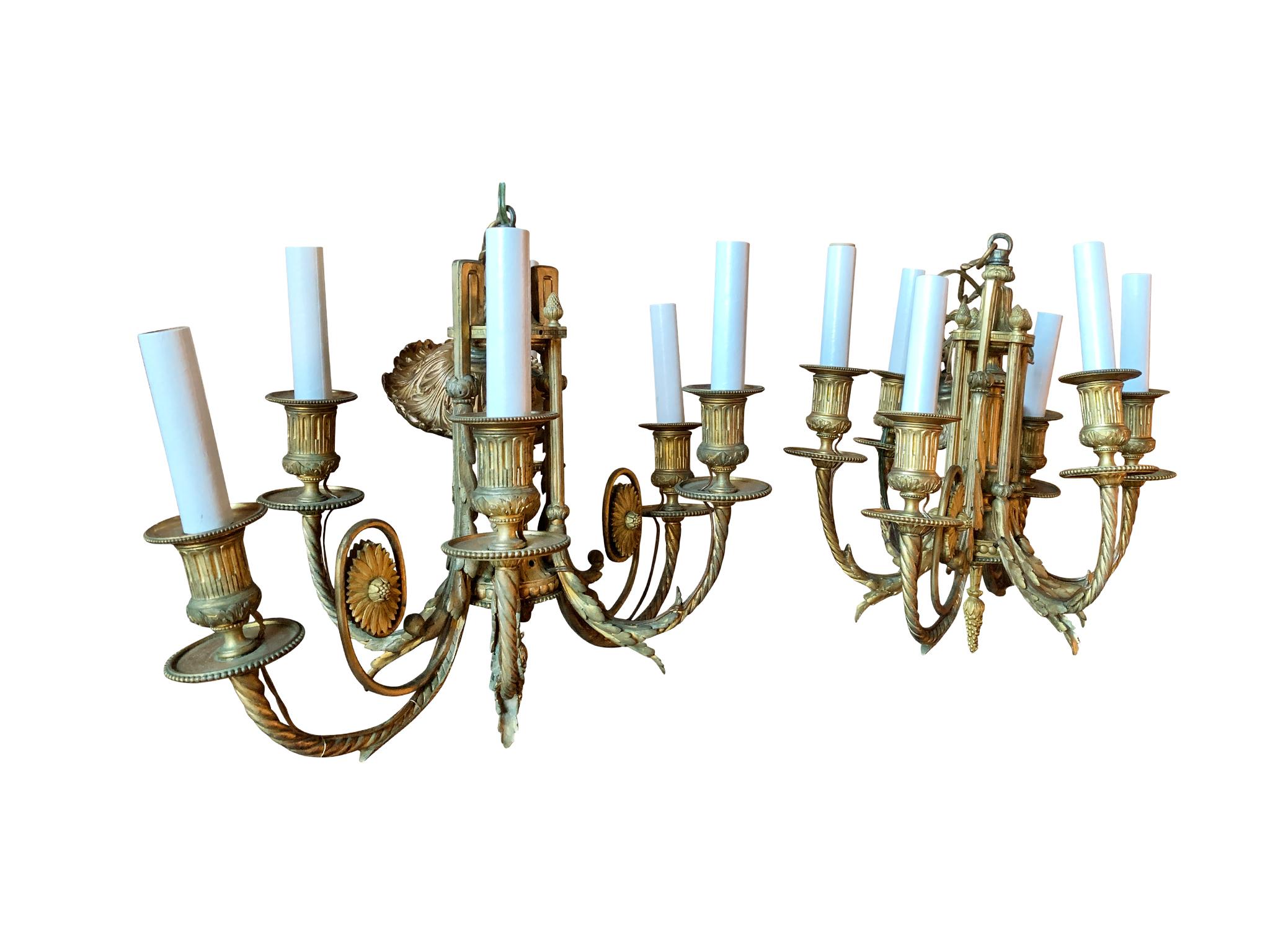 Pair of antique French gilt bronze chandeliers in the Neoclassical style, crafted in the Early 20th Century. Beautiful decorative features include floral and leaf motifs. Each chandelier has 6 candlestick style bulb sockets. They are newly rewired