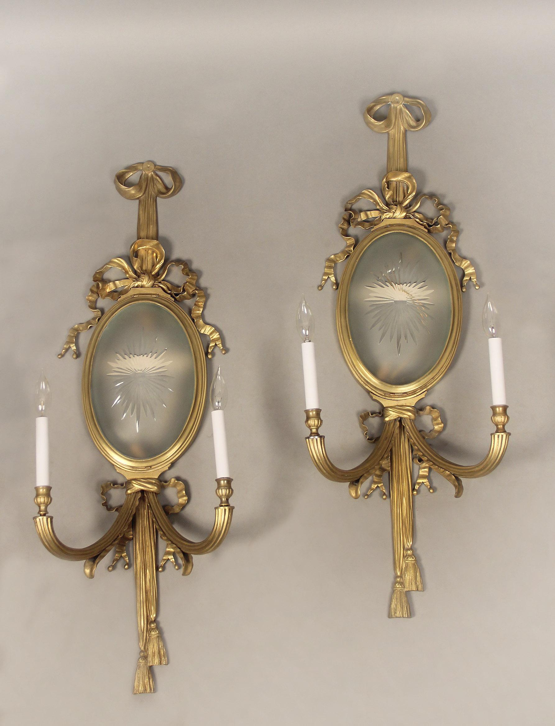A pair of early 20th century gilt bronze four light sconces

Centered with a large etched frosted glass shade, surrounded by tied bows and ribbons, two lights behind the shade and two lit arms.