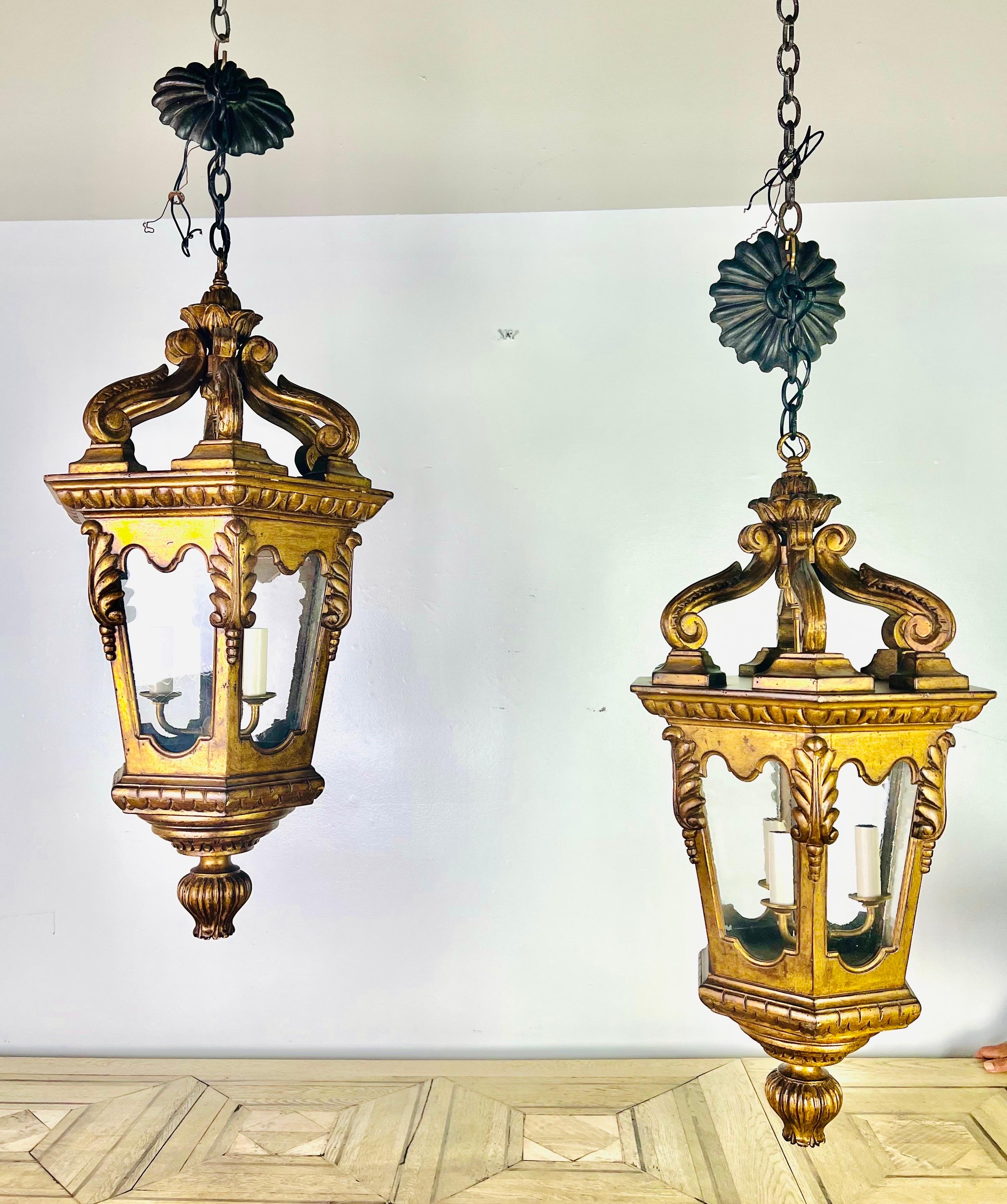 Pair of Italian gilt wood lanterns adorned with carved acanthus leaves and round fluted finials at the base. The glass is original. The 3-light lanterns include chain & canopy and are ready to install.