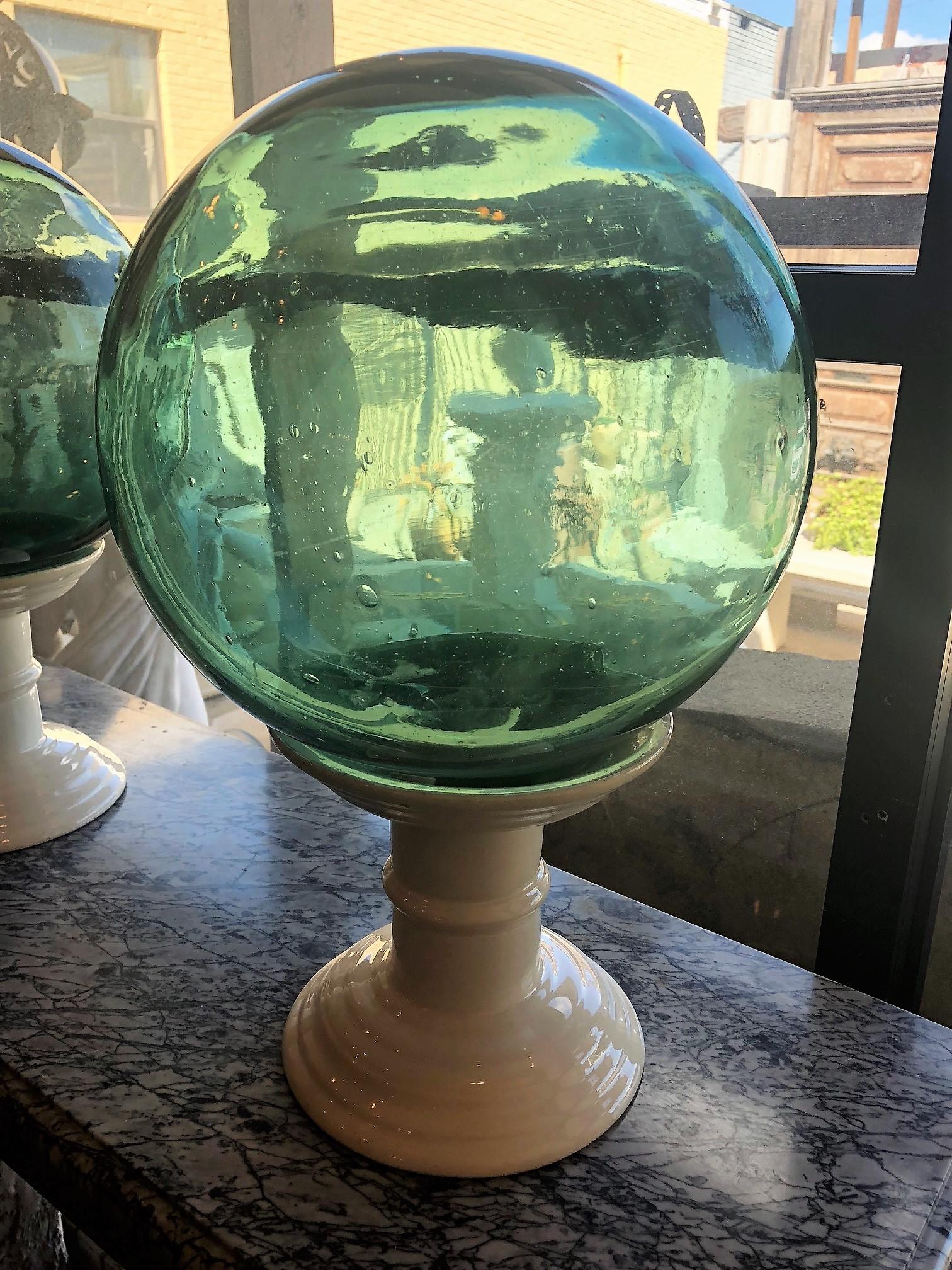 Nous avons le plaisir de présenter cette paire de sphères décoratives en verre soufflé à la main. Les sphères en verre turquois reposent sur des bases blanches 