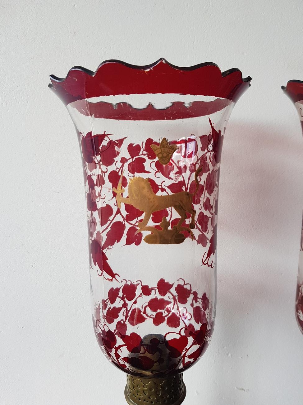 A pair of old hurricane candle lights with glass dome decorated with red floral decoration and gold painted lion the base is made of brass, the candle works with a spring loaded mechanism (the painting has very slight wear and there are a few small