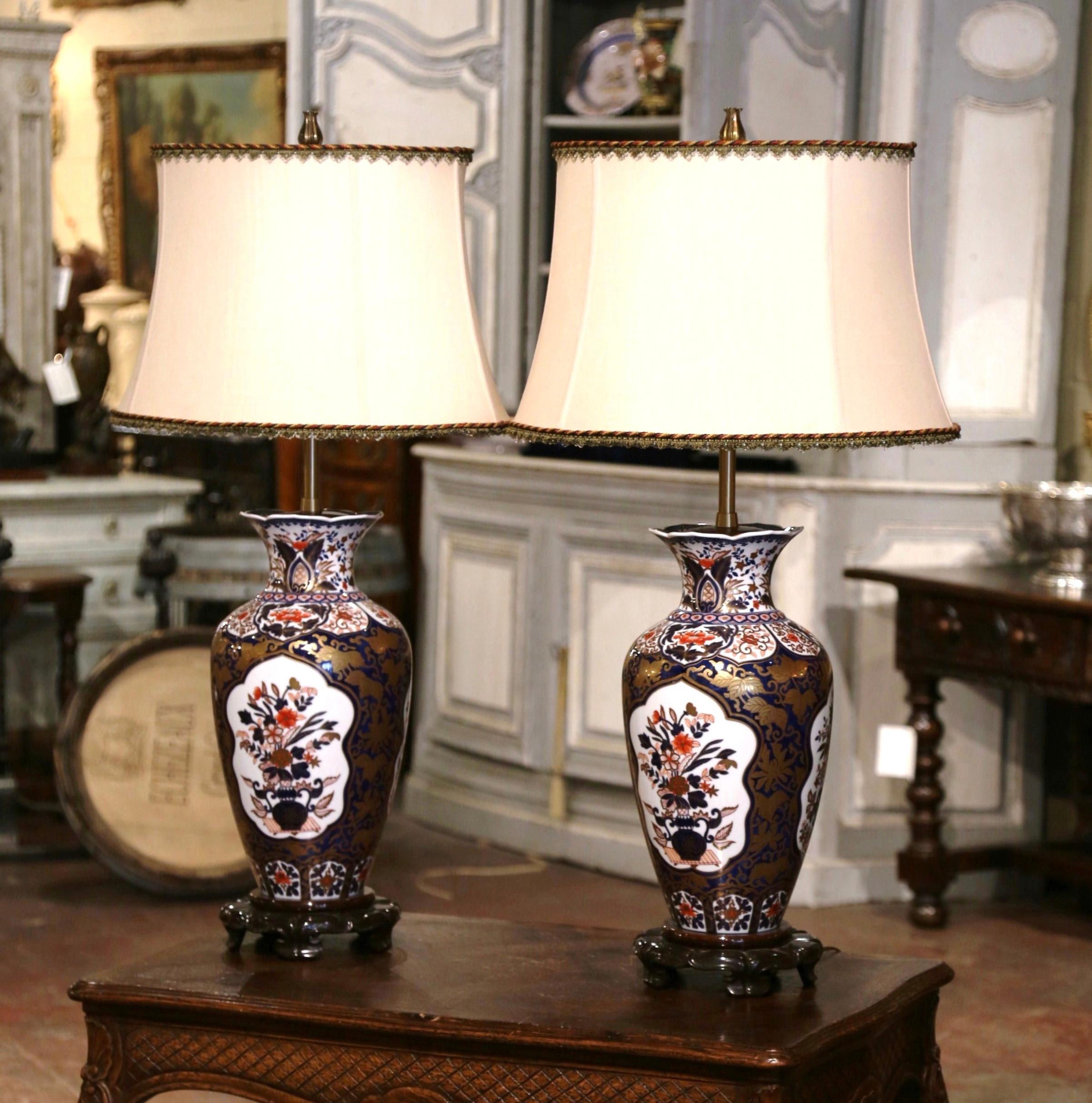 Add the perfect amount of color into your home with this important pair of antique lamps. Created in Japan circa 1934, and round in shape each porcelain lamp rests on a wood base, and is decorated at the neck with a brass mount. The ceramic vases