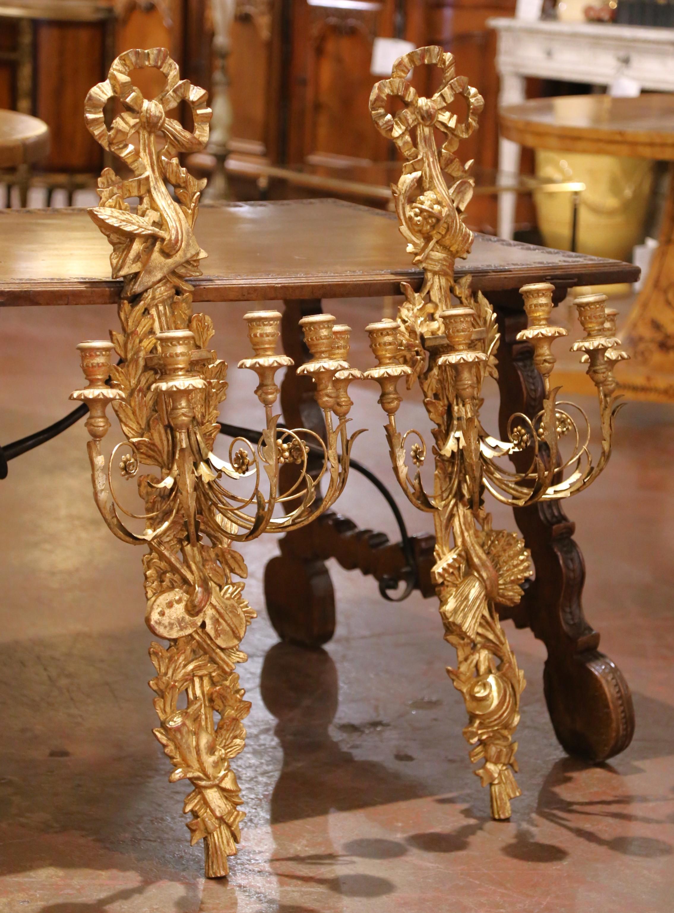 Fabriquée en Italie vers 1920, cette impressionnante paire d'appliques murales hautes incarne la symétrie et le raffinement du style Louis XVI. Chaque applique présente une plaque arrière allongée en bois doré, surmontée d'un nœud de ruban sculpté