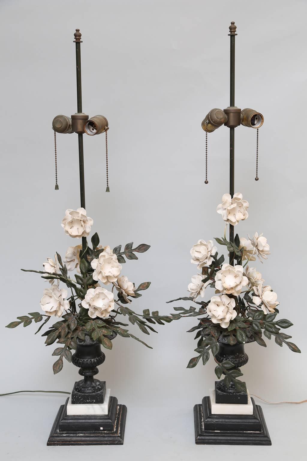 Pair of table lamps, each having a floral bouquet, of handwrought tole, fashioned as blooms and vines, inside a cast urn campana urn, on graduated square plinth. 

Stock ID: D1318.