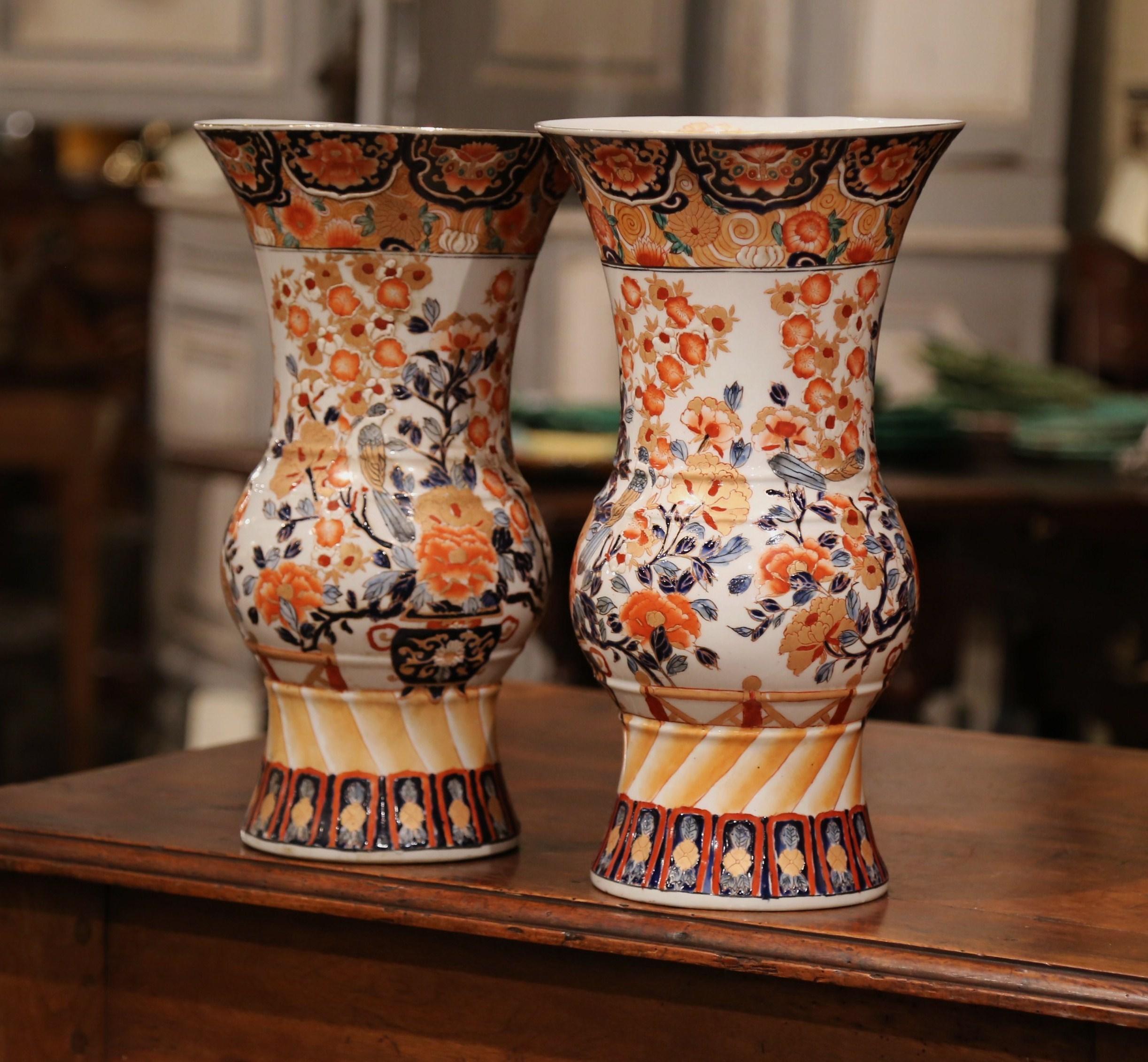 These tall antique porcelain Imari vases were created in Japan circa 1920. Each ceramic vessel has a wide mouth at the top, a rounded body, an elevated base, and hand painted with exotic, Asian bird and floral decor in delicate blue and pastel