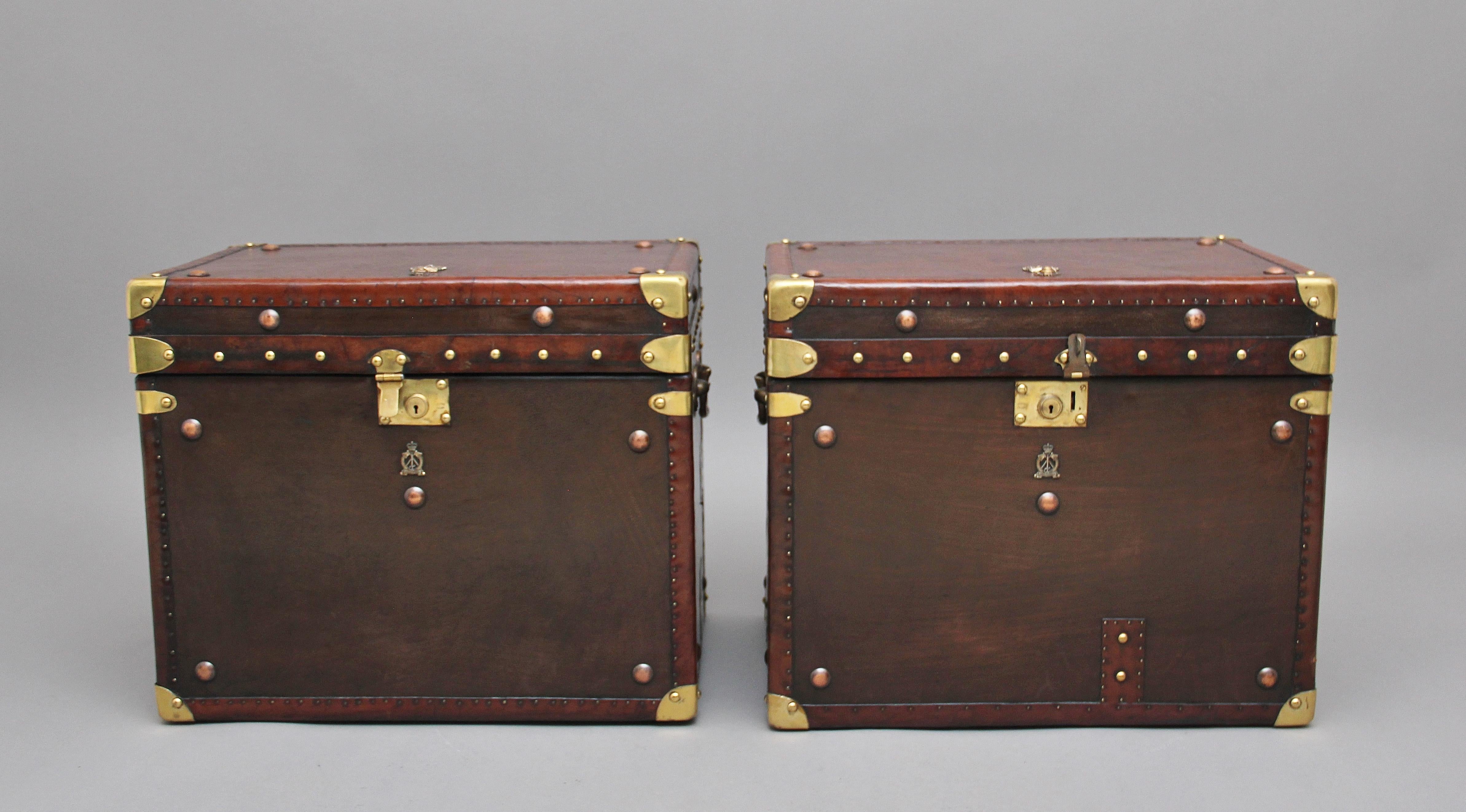 A fabulous pair of early 20th century leather bound ex army trunks with brass straps and corners, copper studs and brass carrying handles on the sides, the trunks opening to reveal a nice dark blue lined interior, on the top and front of the trunks