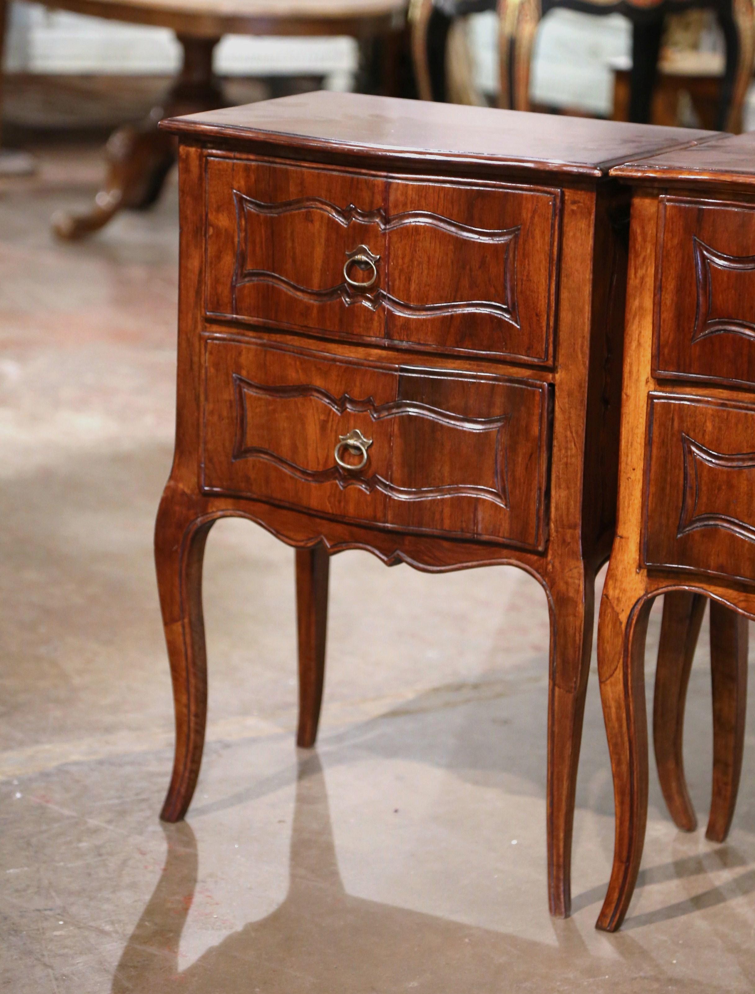 Decorate a master bedroom with this elegant pair of antique bedside tables. Created in France, circa 1920, each fruitwood cabinet stands on cabriole legs over a scalloped apron. The nightstand features two bombe drawers decorated with hand carved