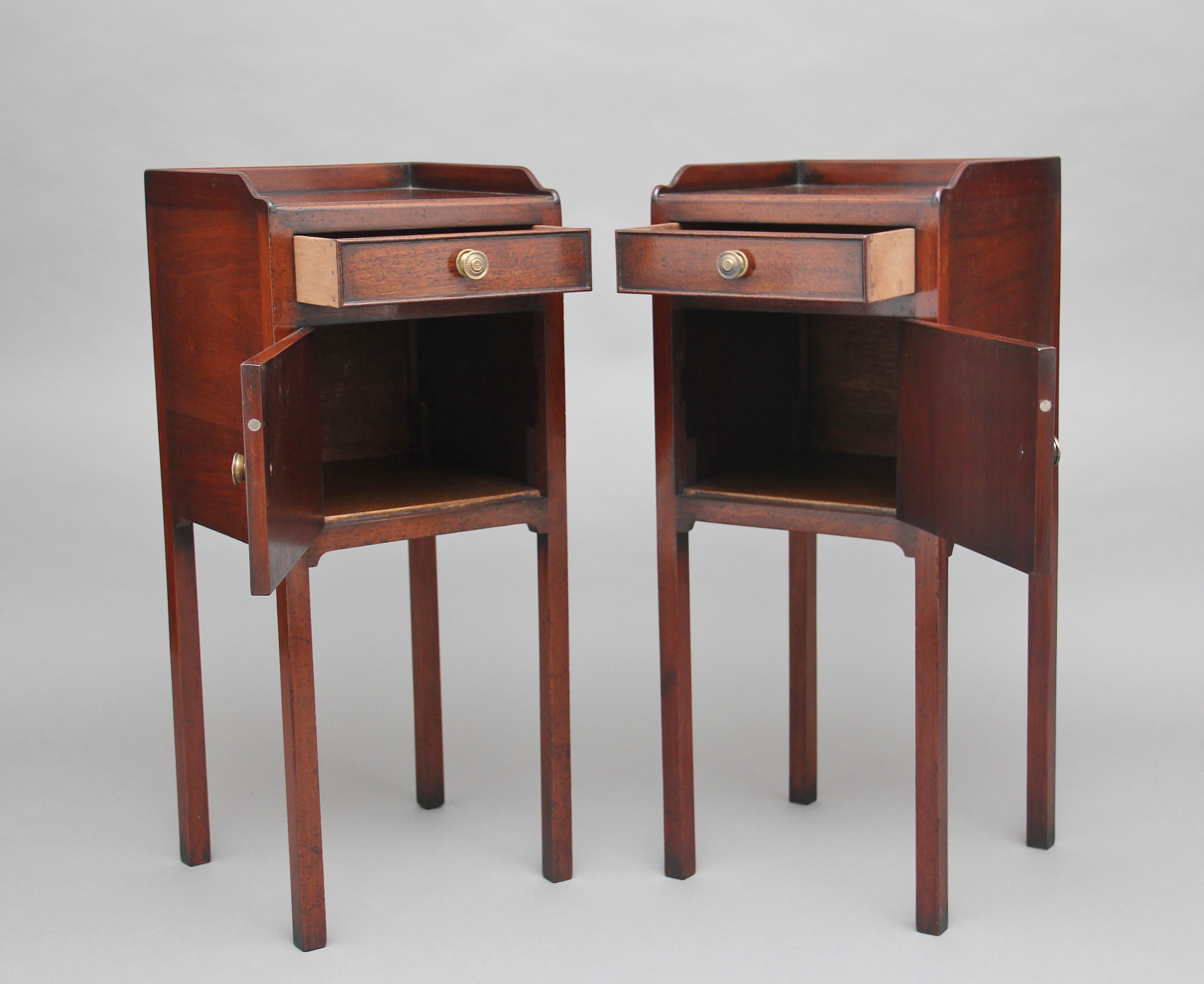 A nice pair of early 20th century mahogany bedside cupboards, the tops having a gallery running along the sides and back, the front of the cupboards having a single drawer above a hinged cupboard door with brass turned engraved handles, supported on
