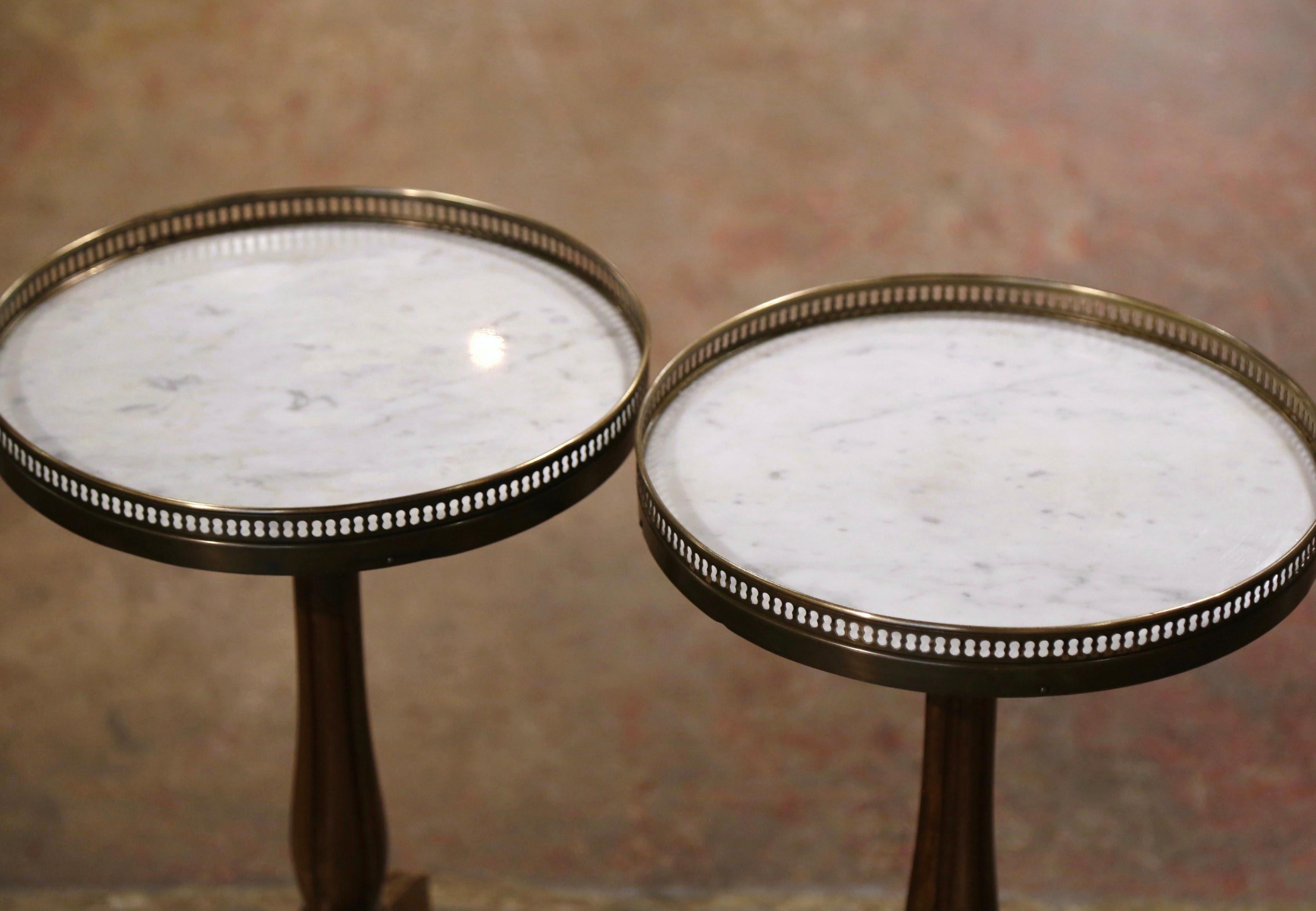 Decorate a den or living room with this elegant pair of antique side tables. Crafted in France, circa 1920, each table stands on a carved fluted pedestal base ending with three curved legs; the surface is dressed with a white and grey inset marble