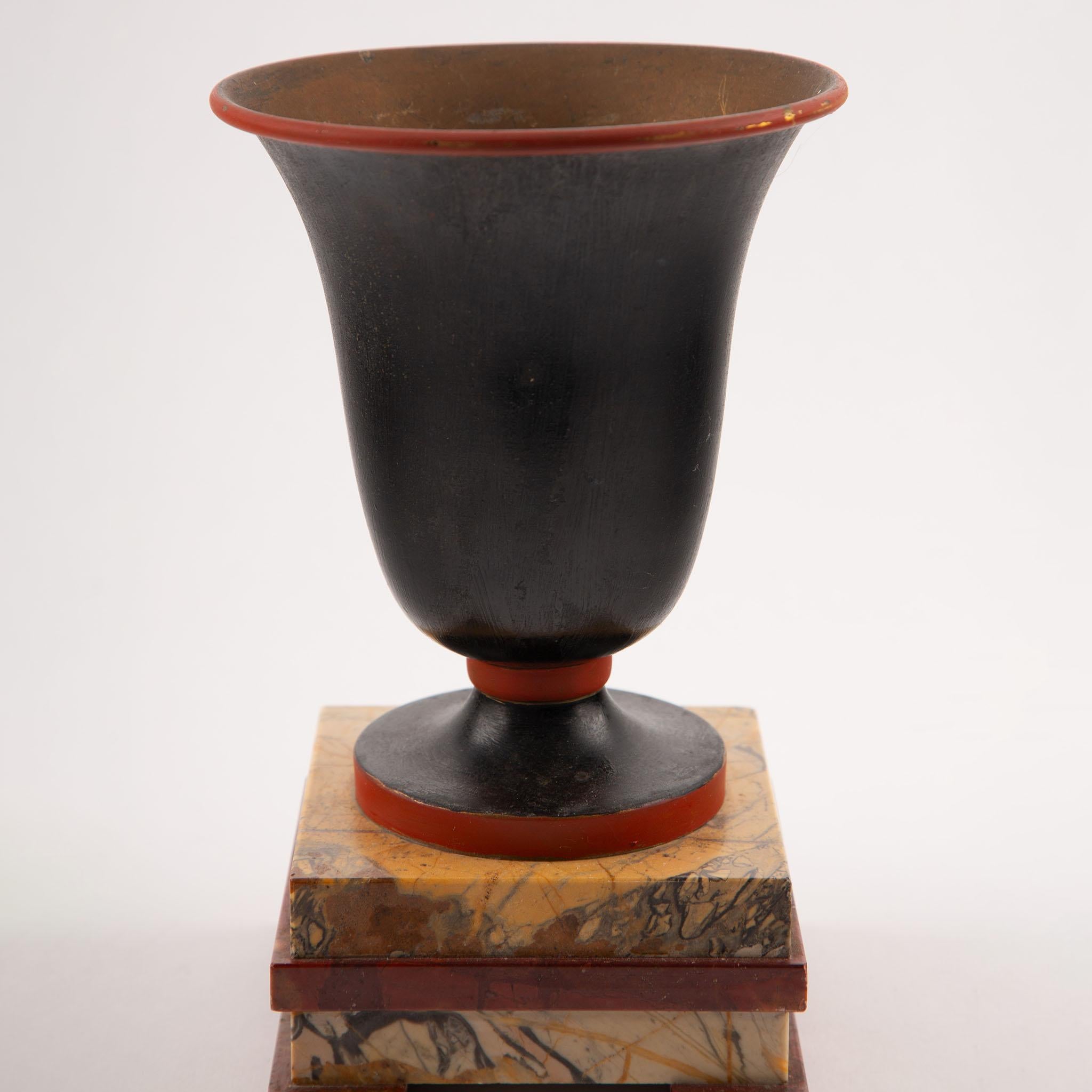Pair of Tôle Urn-Form Vases on Marble Plinths, Early 20th Century
Hand-formed from rolled tôle (painted sheet iron), each campana-shaped vase rises to a crisp, flared rim and is finished in a deep matte black patina highlighted by terracotta-red