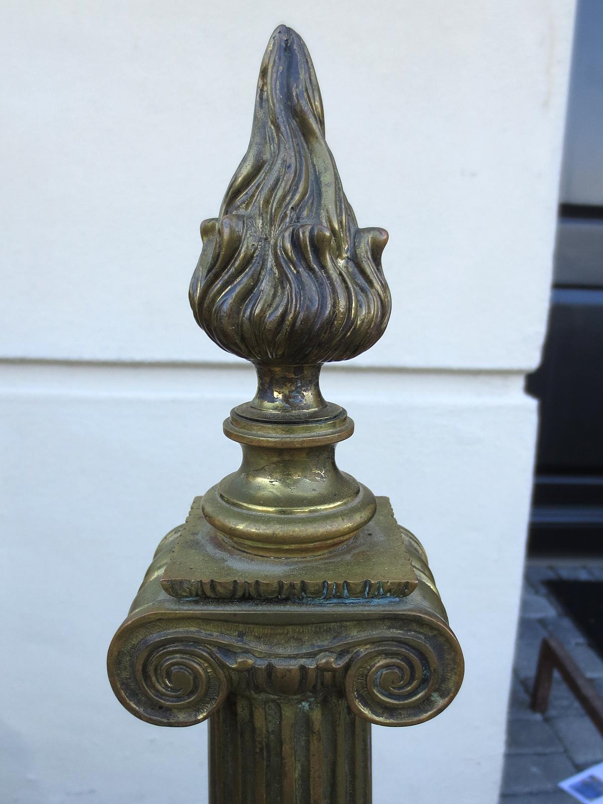 Pair of early 20th century neoclassical brass andirons with flame finials, column shaft.