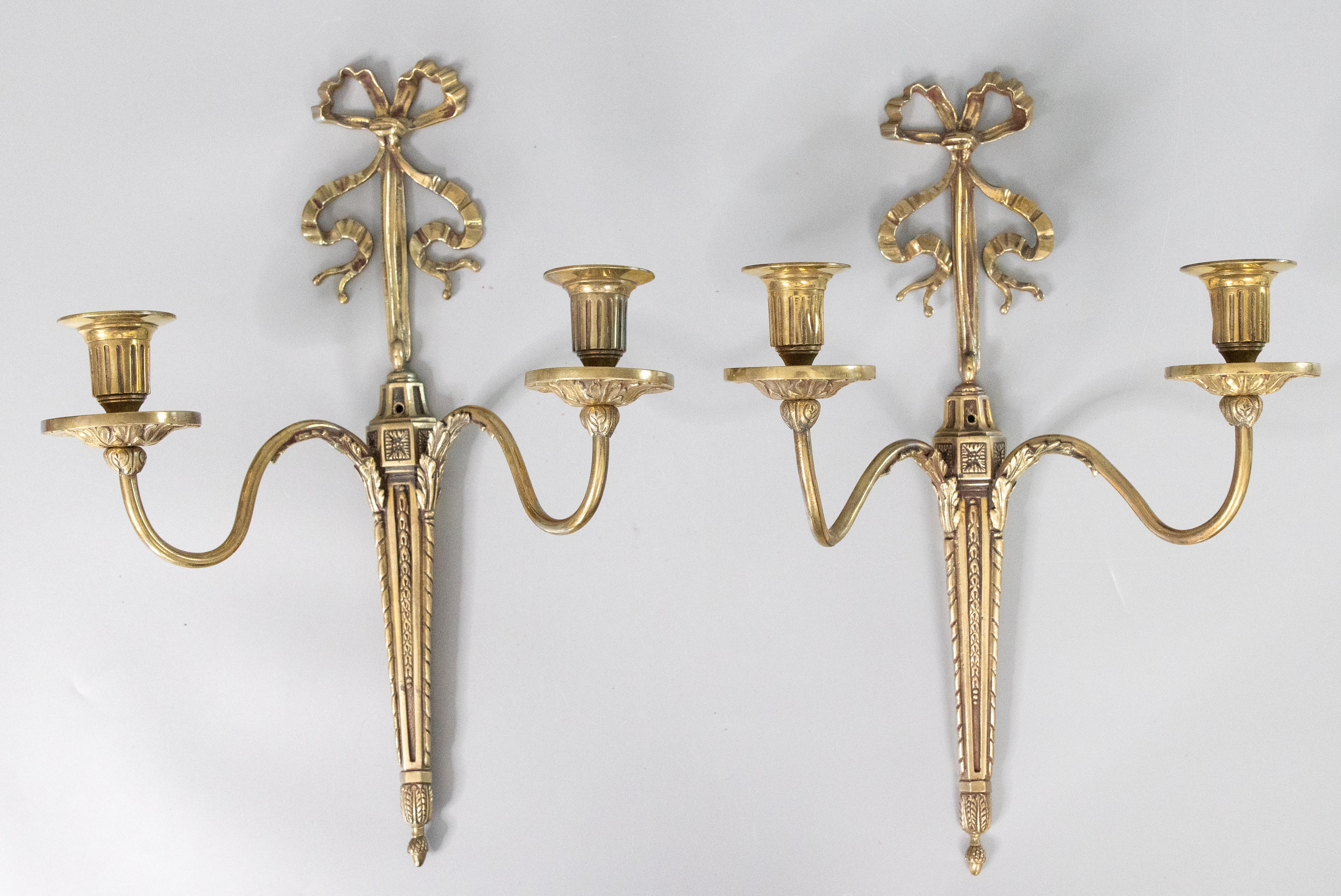 Preciosa pareja de antiguos apliques de pared de dos brazos de latón de estilo neoclásico francés de principios del siglo XX. Estos preciosos apliques están decorados con hojas de acanto, detalles florales, lazos y cintas en una preciosa pátina de