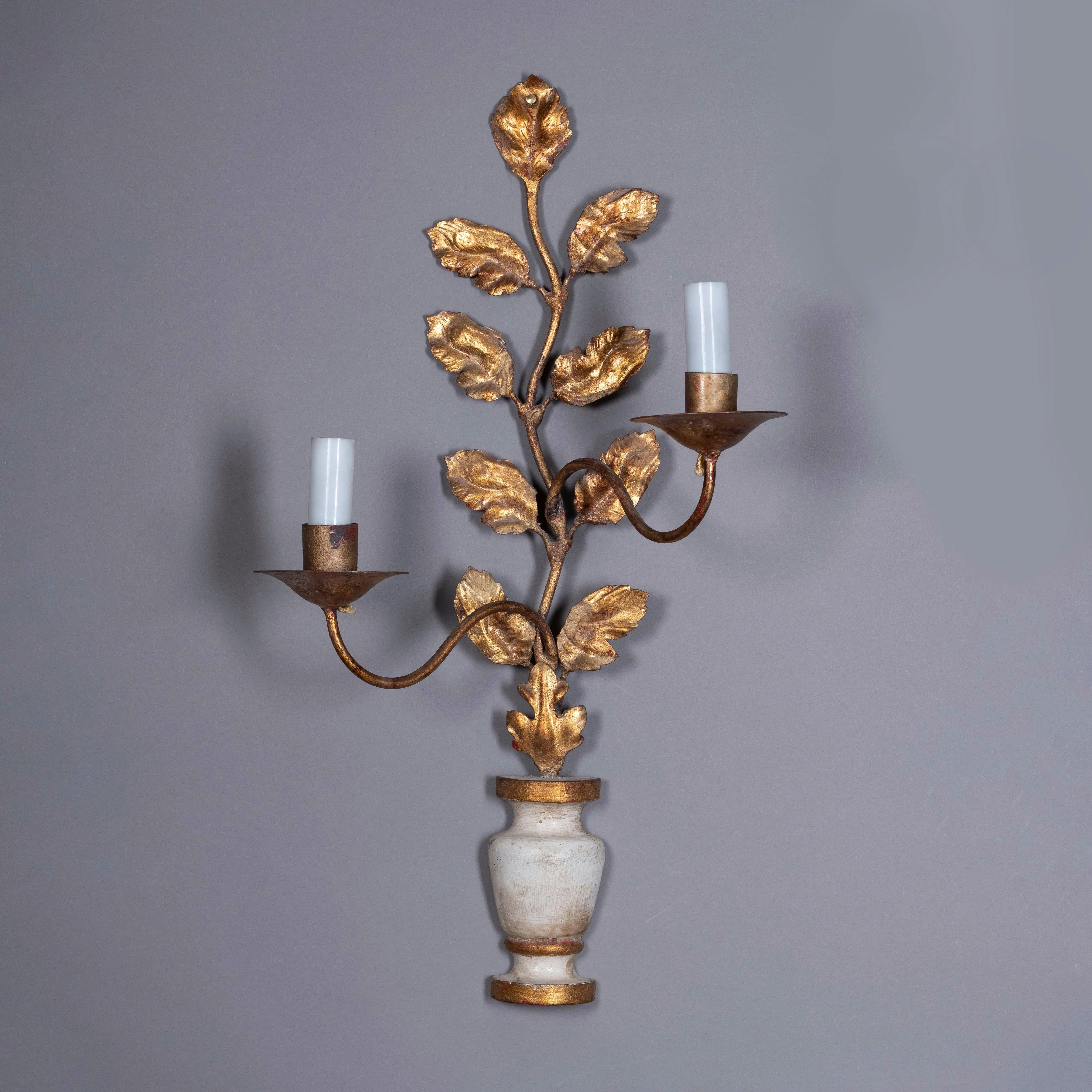 A pair of early 20th century wall lights, each with a gilt metal foliate back and two scrolling candle arms issuing form a painted and parcel gilded vase.
