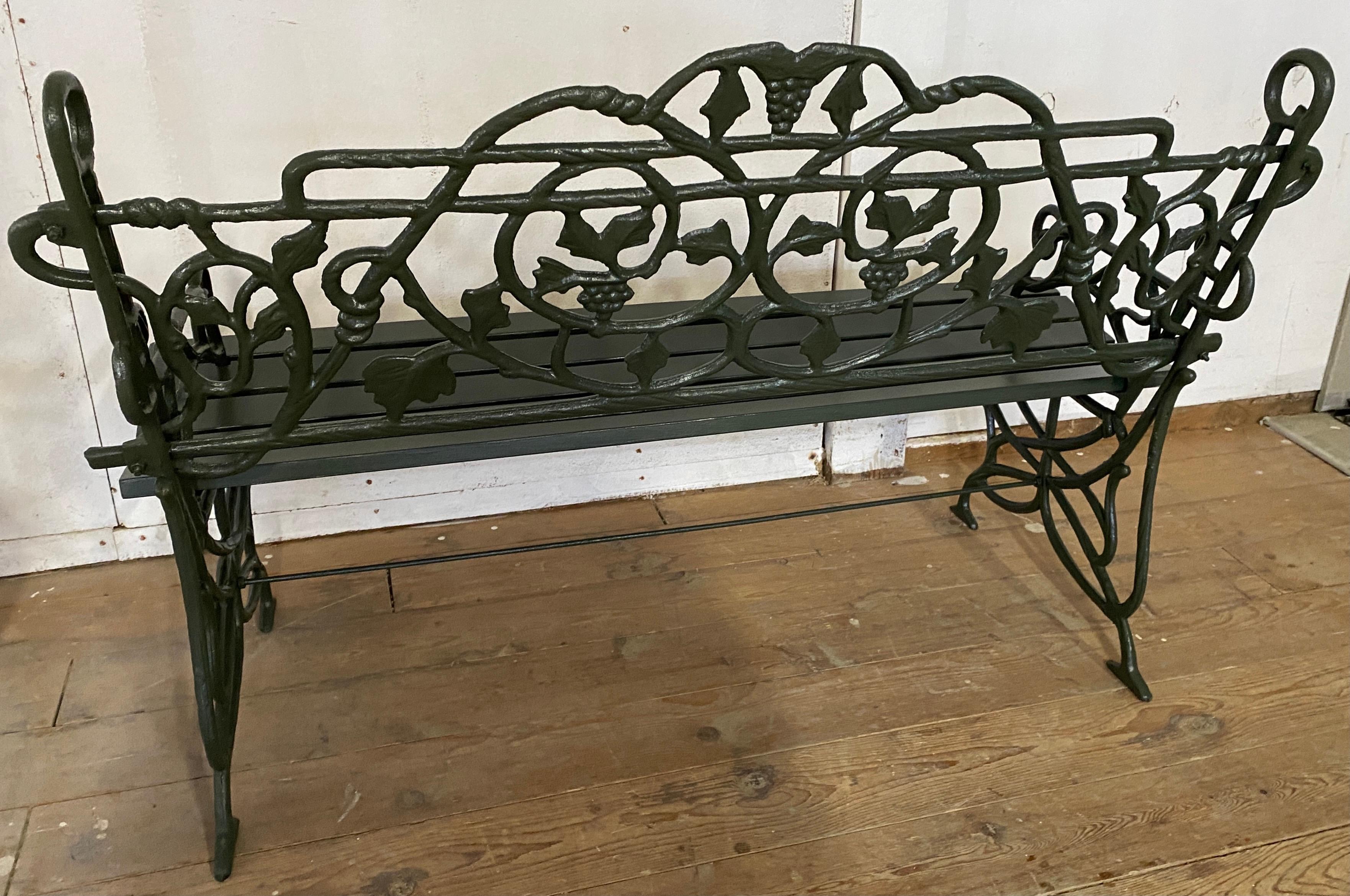 Pair of cast iron benches standing on carved scrolled painted iron supports with backs decorated in trailing grape leaf and vine motif. Newly re-painted and restored, ready to be placed in any garden or outdoor area for a dramatic
