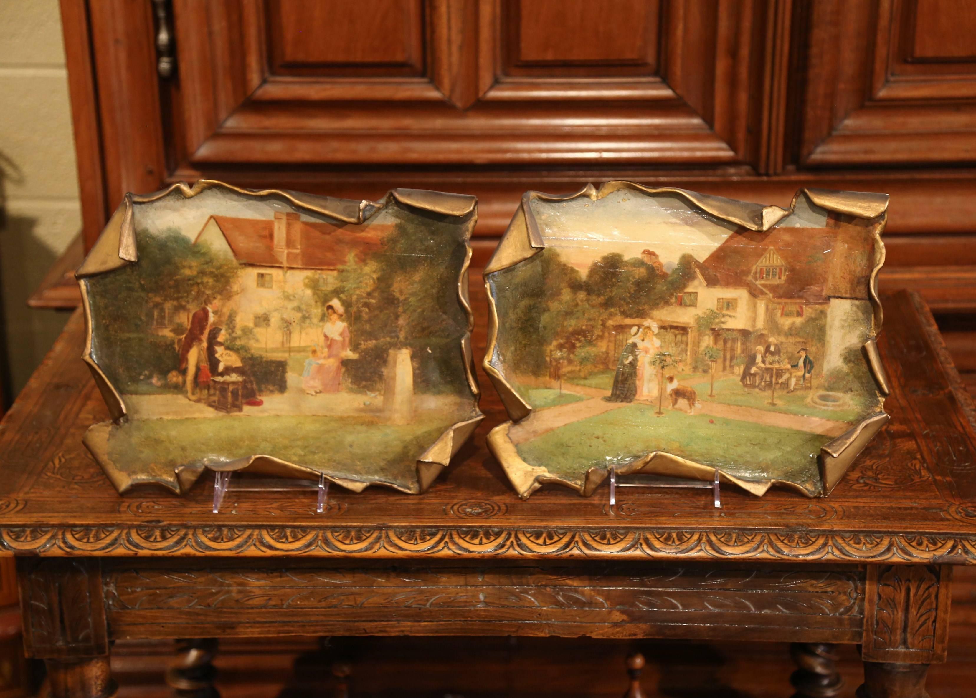 This interesting pair of antique wall hanging paintings on board was created in France, circa 1920. Made of paper-mache, each art work with curved edges, features an outdoor pastoral scene with people and children gathering. Each decorative painting