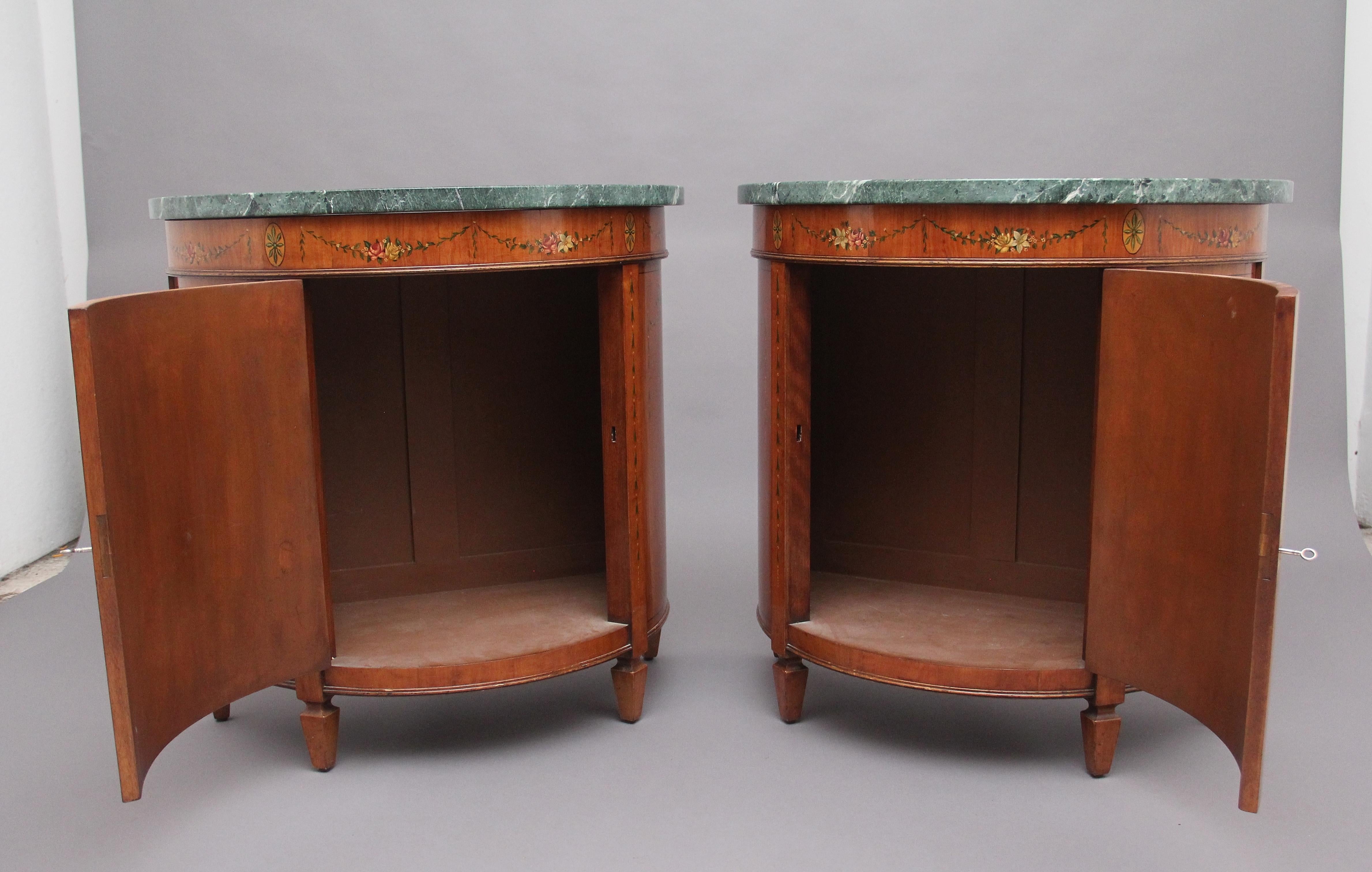 A fabulous pair of early 20th century satinwood and painted demi lune cabinets in the Sheraton style, having the original turquoise veined marble tops above a decorative frieze with painted floral patterns and oval panels, the shaped single door