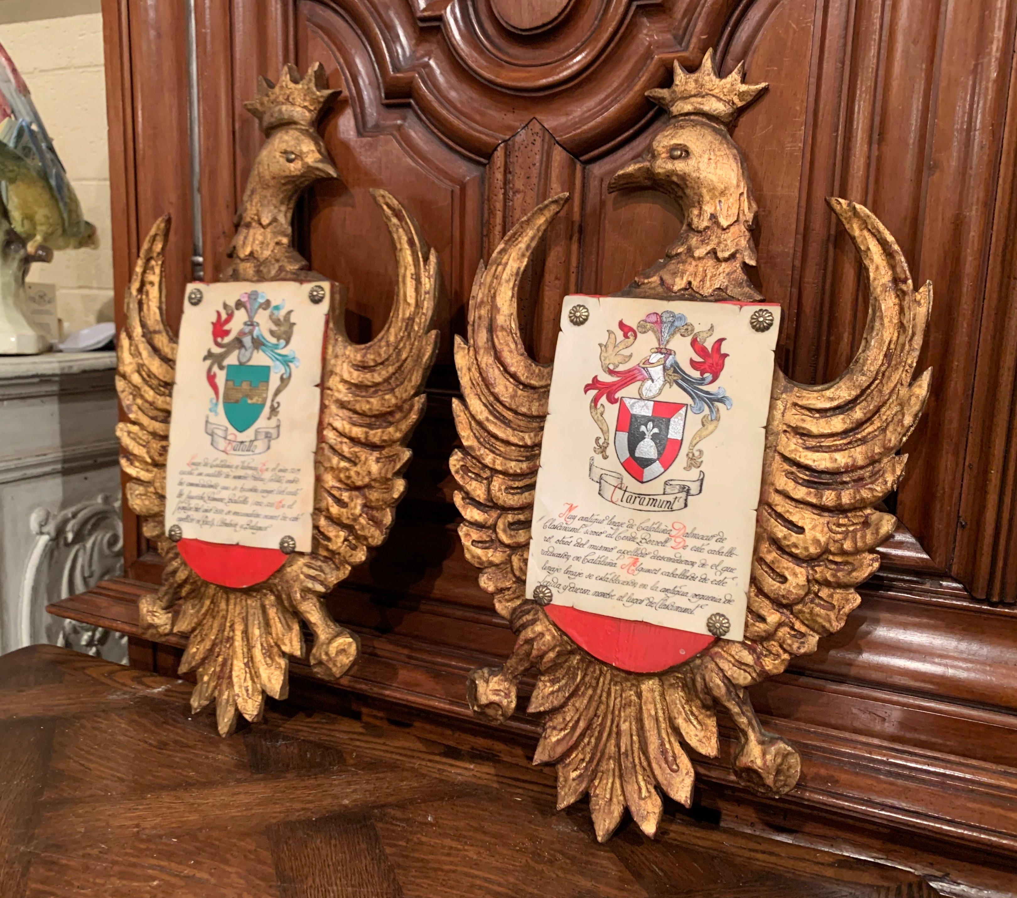 Decorate an office or a study with this colorful pair of antique medieval crests; crafted in Spain circa 1920, each shield depicts an hand carved eagle sculpture embellished with an hand written and hand painted parchment paper with coat of arms