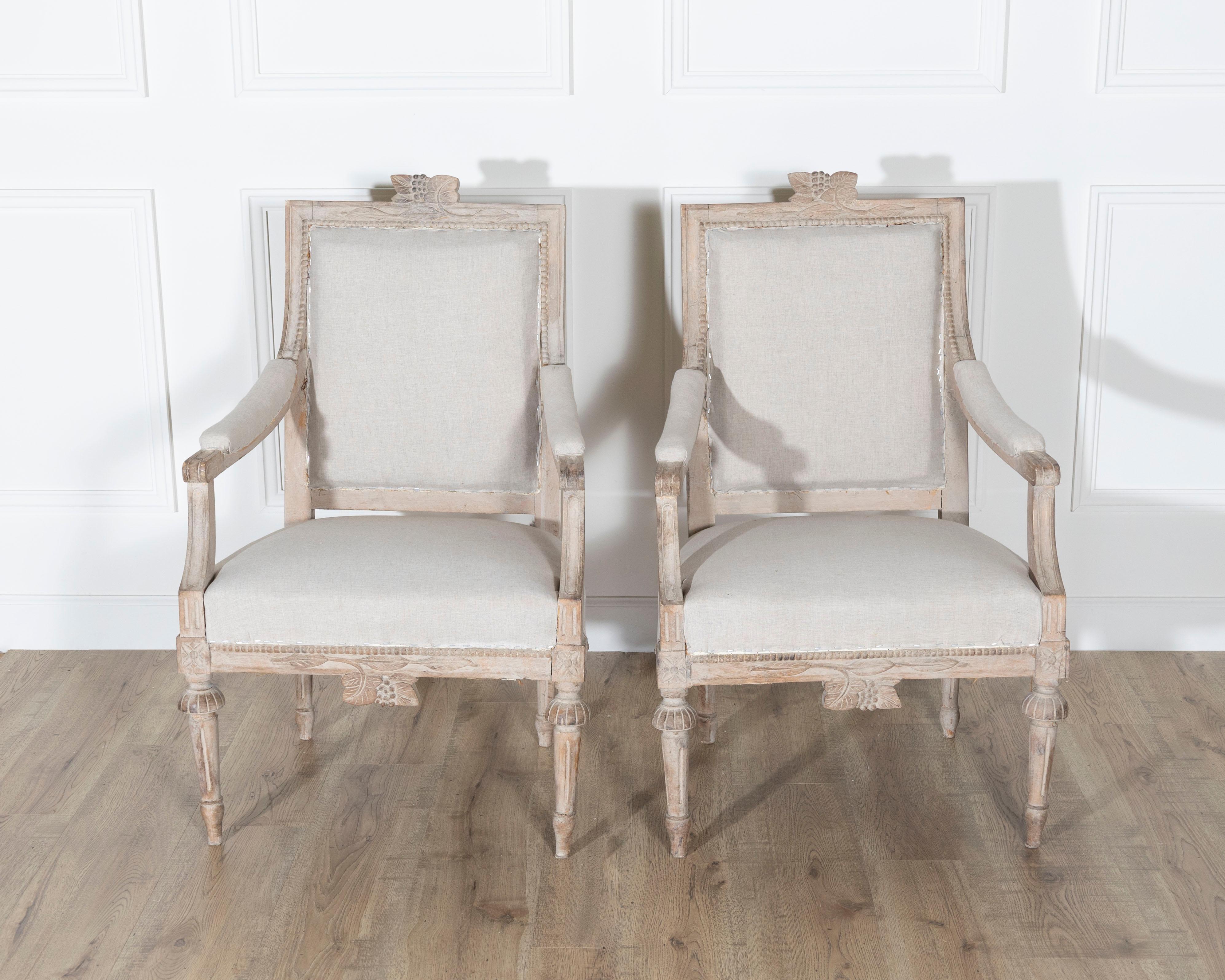 A wonderful pair of Gustavian style armchairs from Sweden, dating to the early 20th century, masterfully carved and full of timeless neoclassical elegance. Each chair features a square backrest topped with a decorative crest of carved ribbons and